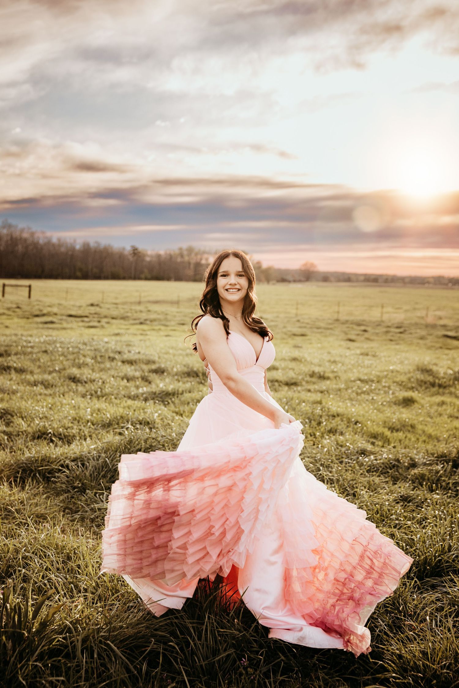Woman in flowing ombre pink dress twirling in sunset-lit meadow.
