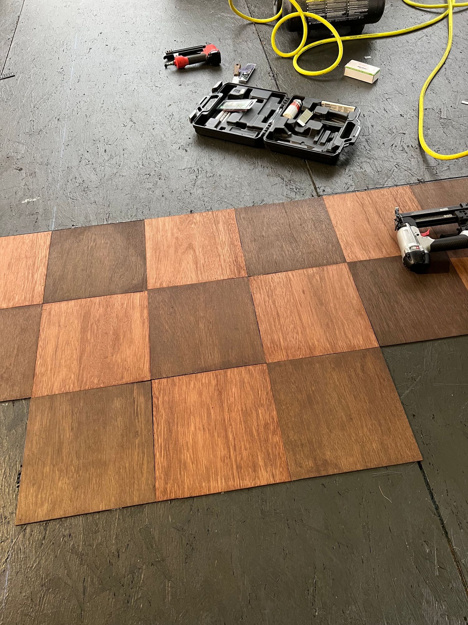 Rows of wood flooring or planks being installed on a concrete surface with tools and yellow cord visible.