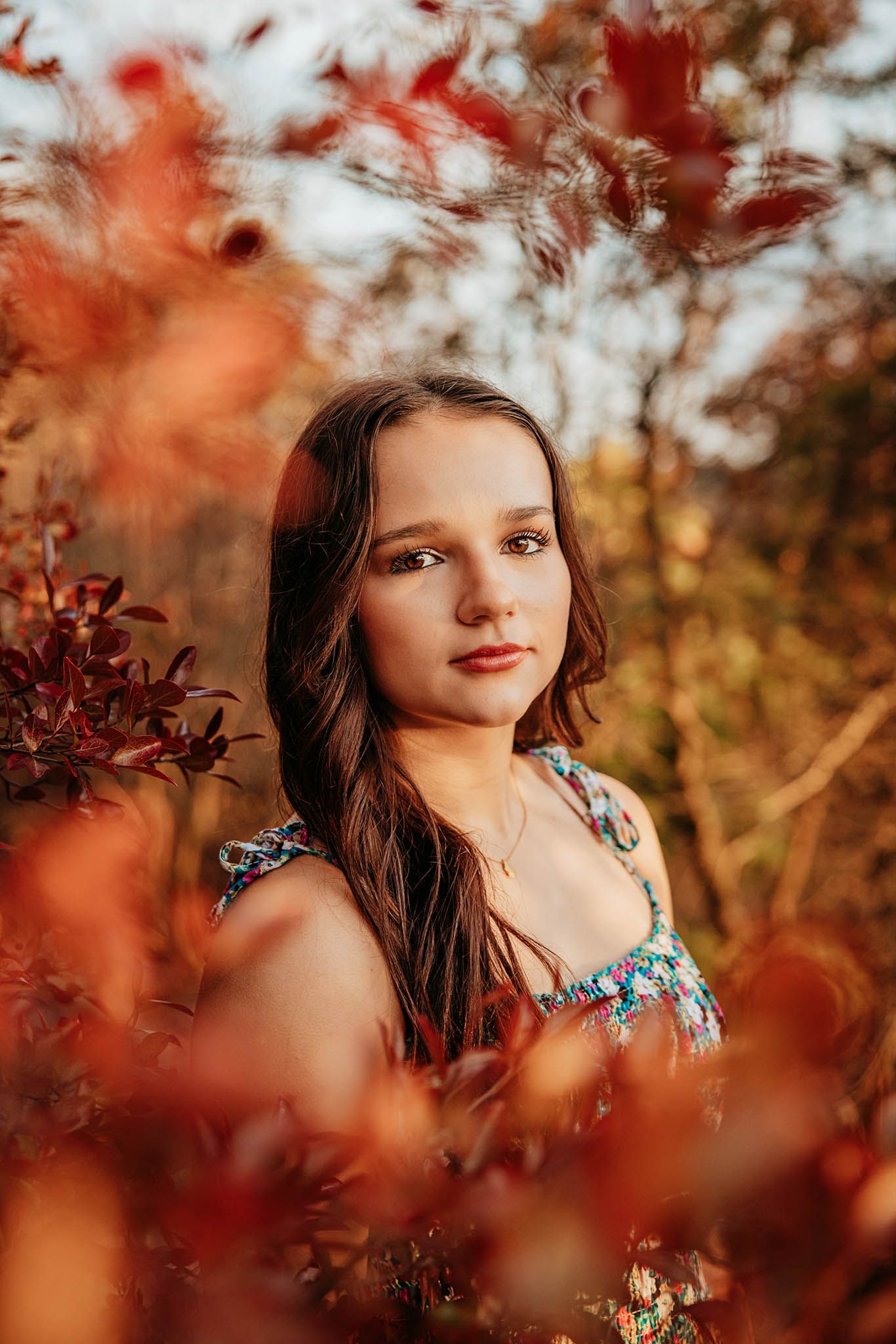 Artistic portrait through autumn red leaves with soft bokeh effect.