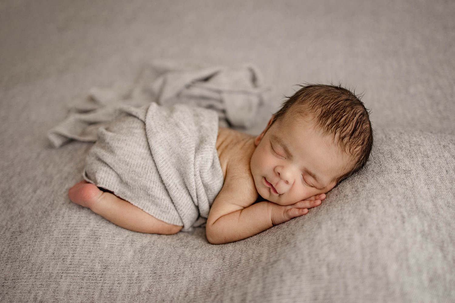 Sleeping newborn photographed in soft gray tones on textured blanket in artistic composite.