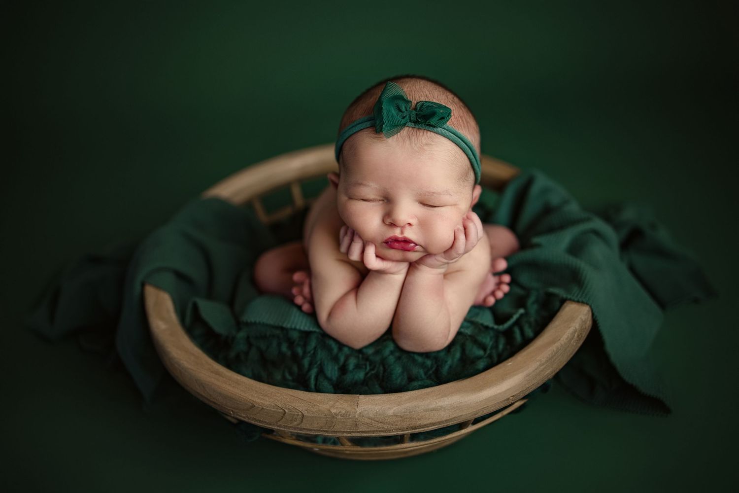 Artistic newborn photography series with baby posed in dark green setting with wooden props.
