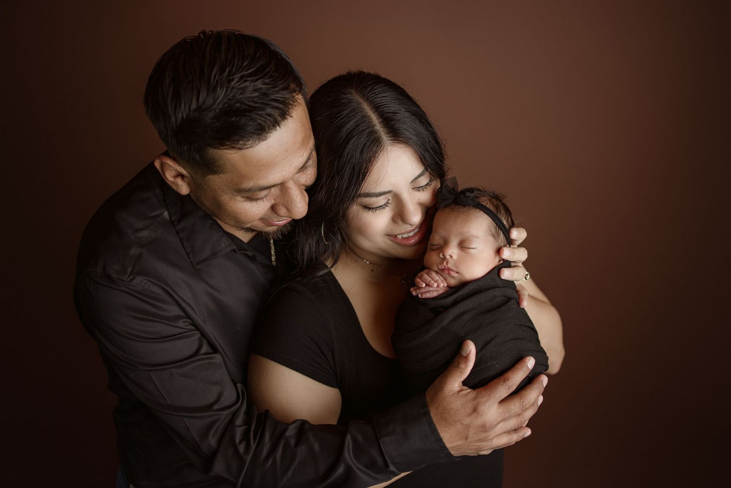 Intimate newborn photography session with dark brown studio backdrop.