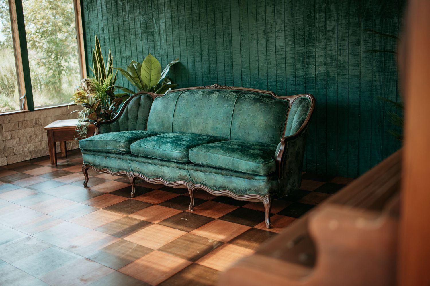 Vintage green velvet sofa sits in sunlit room with wooden floors and teal walls.