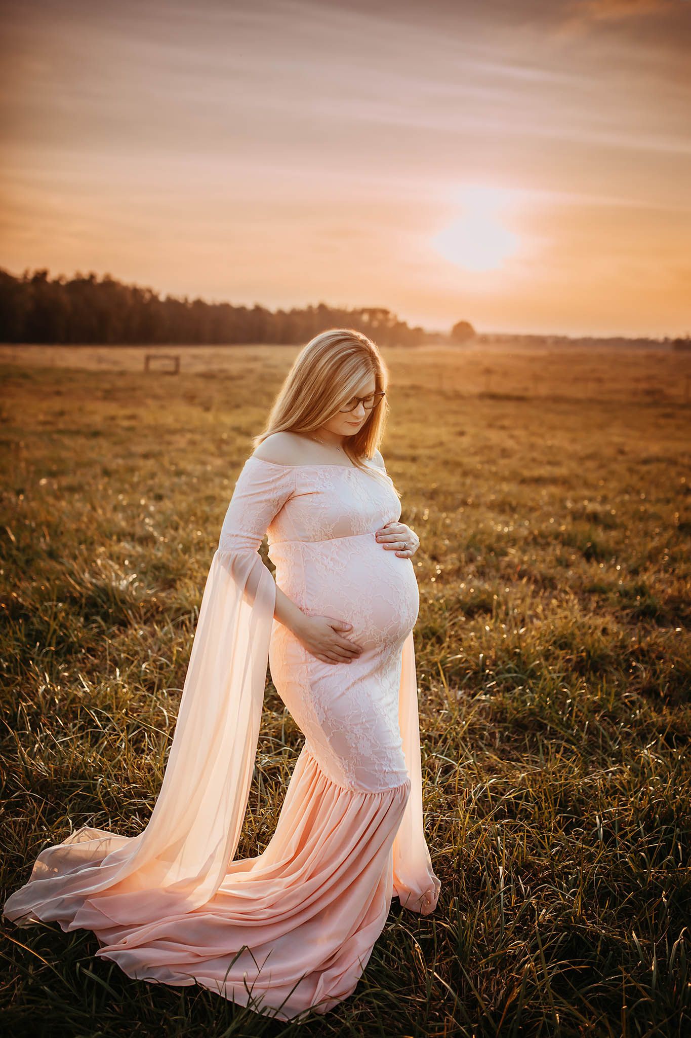 Ethereal maternity photoshoot in a golden field at sunset with flowing fabric.