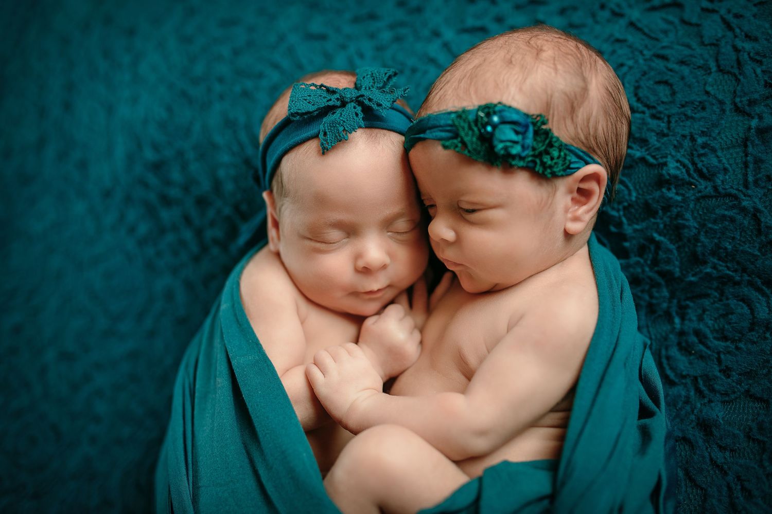 Two newborns swaddled in teal fabric sleeping peacefully together.