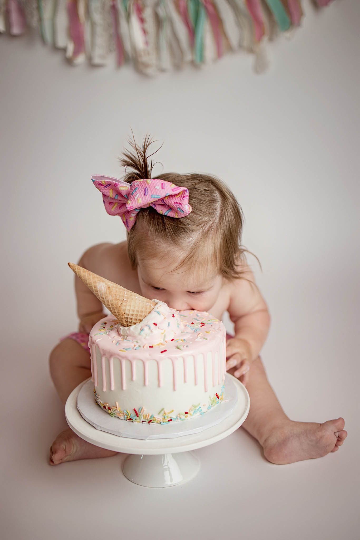 Baby having cake smash photo session with pink and white decorated cake.