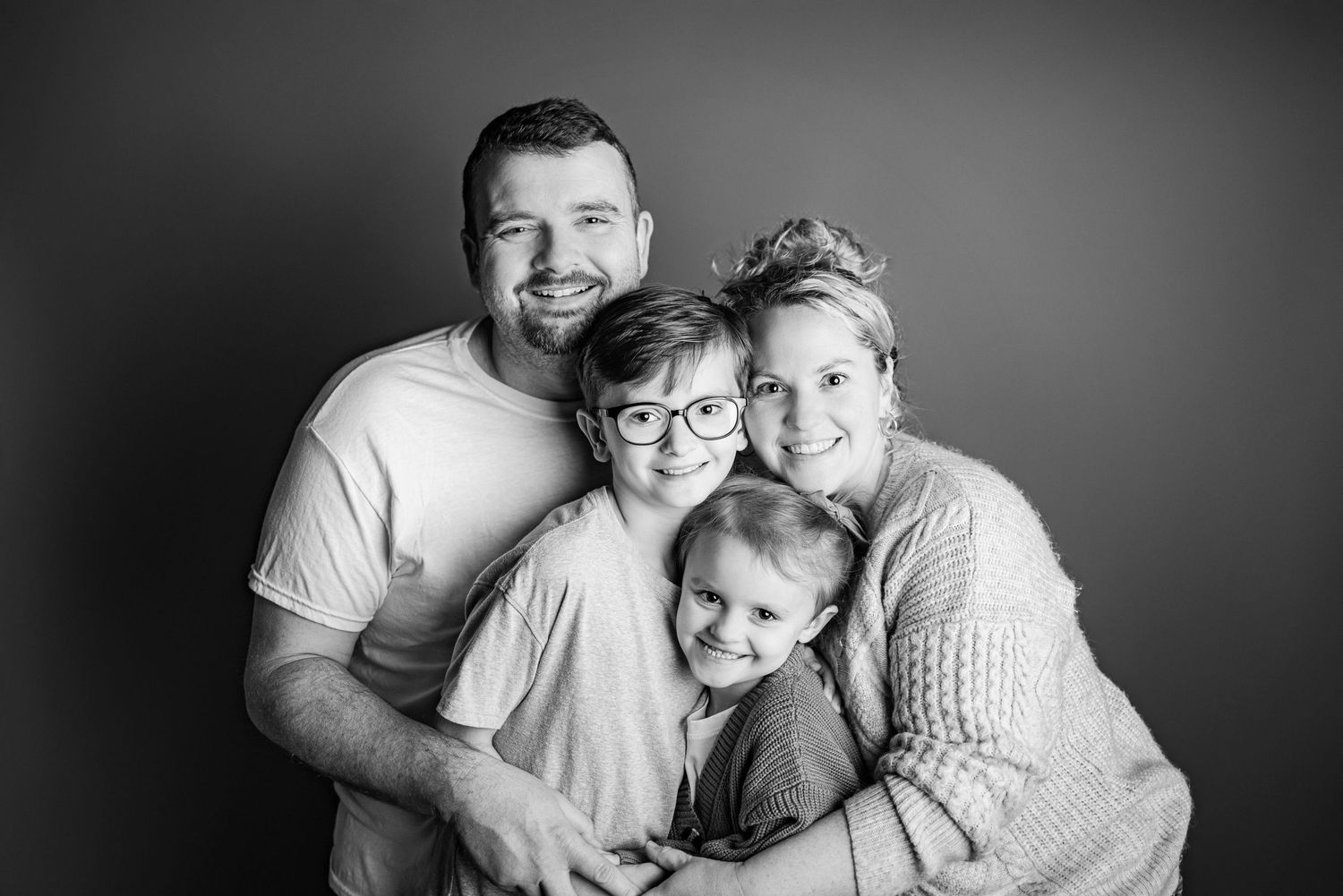 Black and white family portrait series showing intimate embraces against dark background.