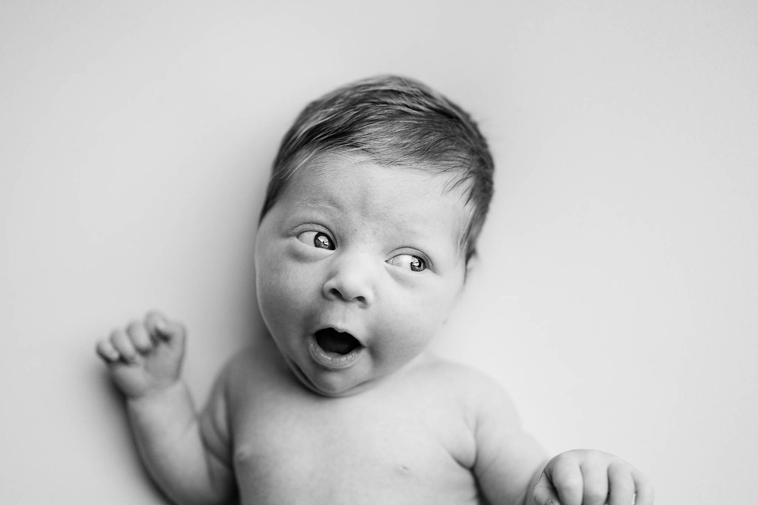 Black and white portrait of expressive baby with wide-eyed surprised expression.