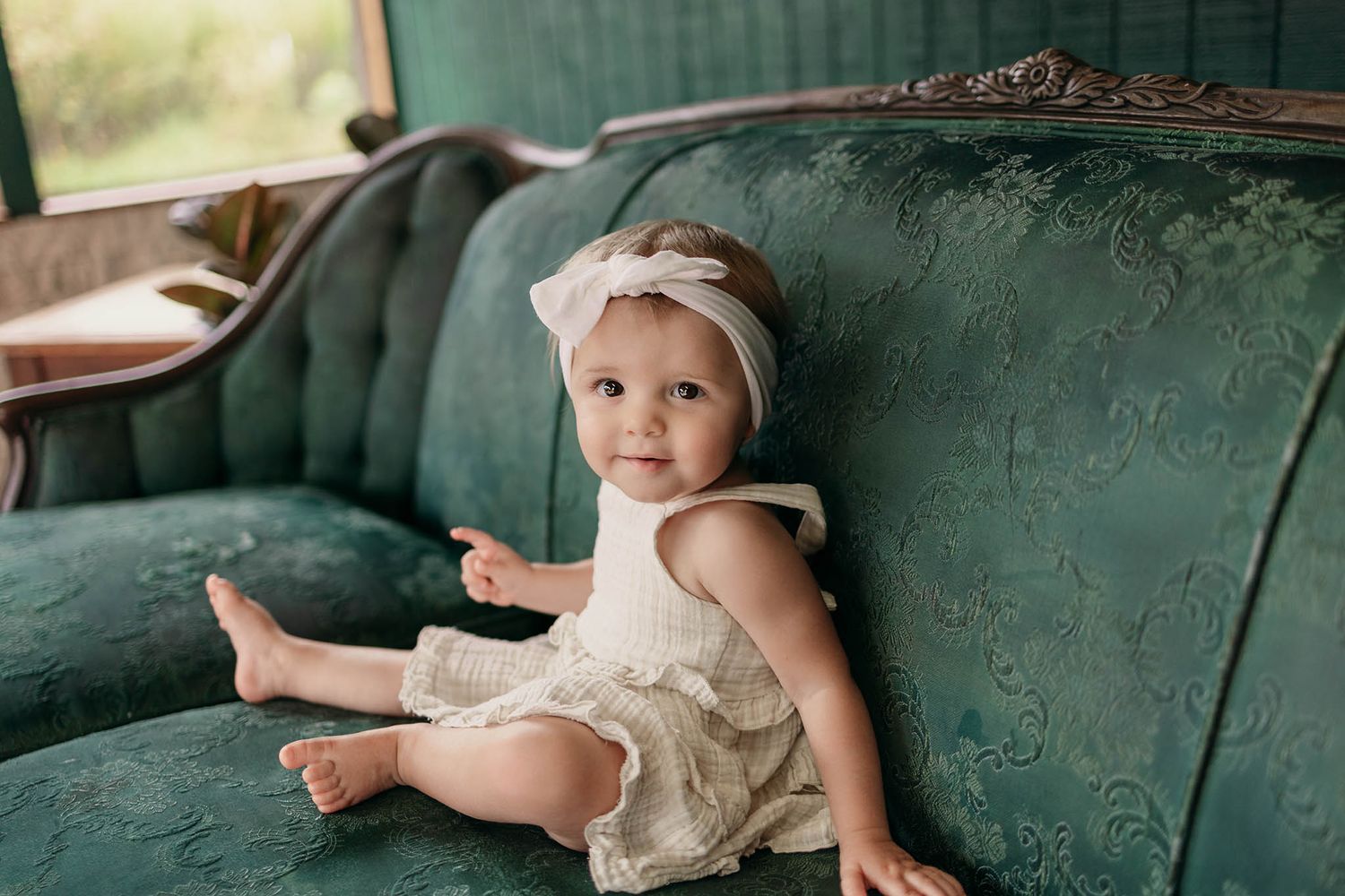 Baby playing on vintage green sofa with distressed upholstery.