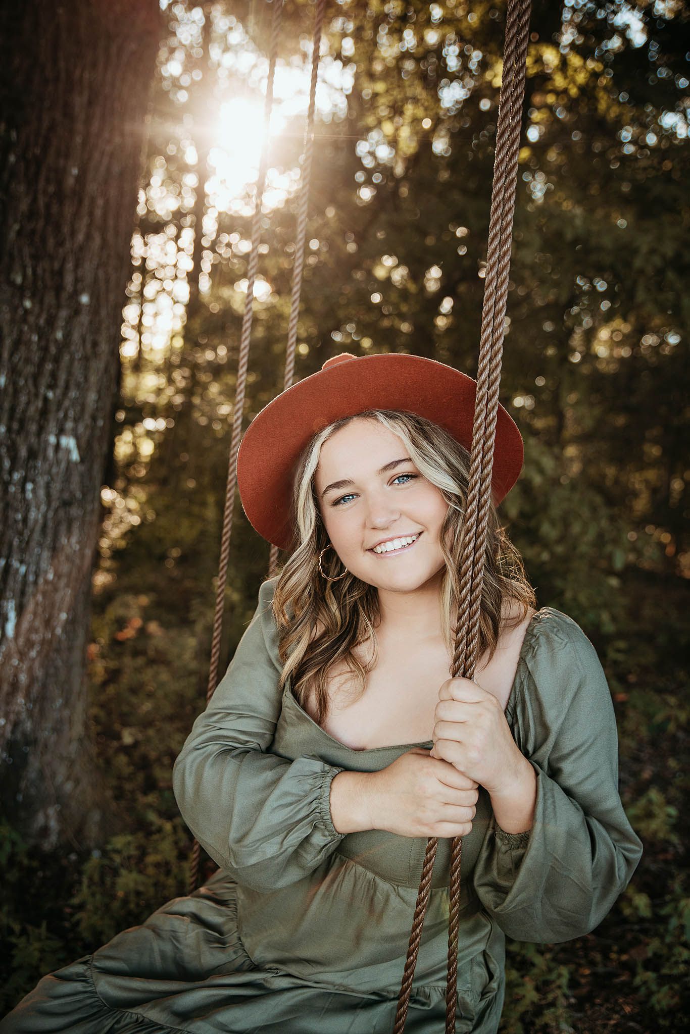 Person in brown hat and green jacket enjoying swing in sunlit forest.