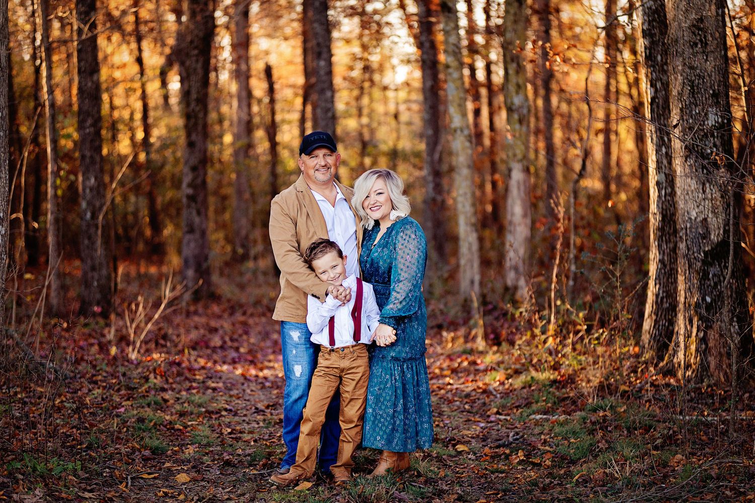 Family portrait session in autumn woods with golden sunlight filtering through trees.