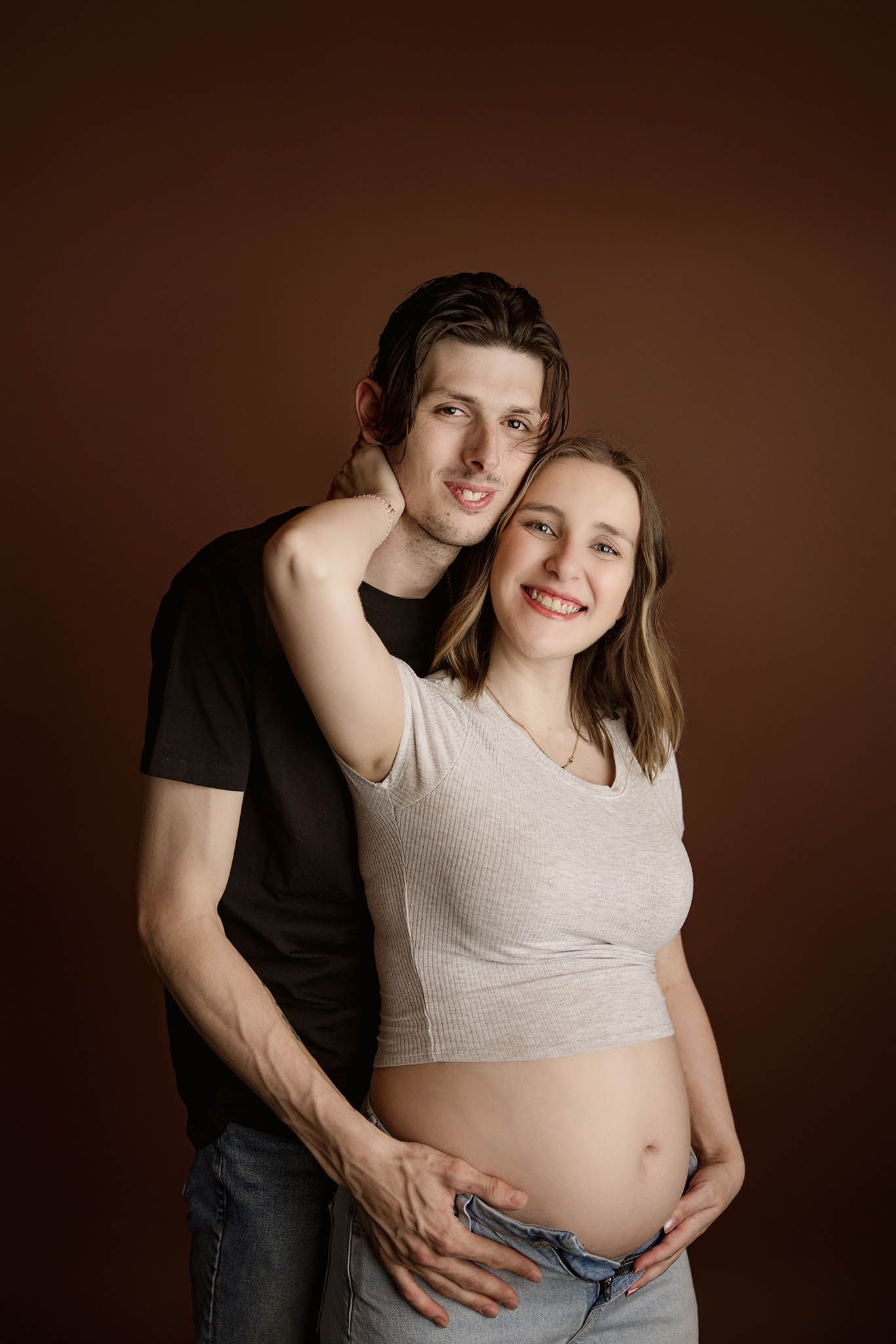 Intimate maternity photoshoot showing a couple embracing against a dark brown background.
