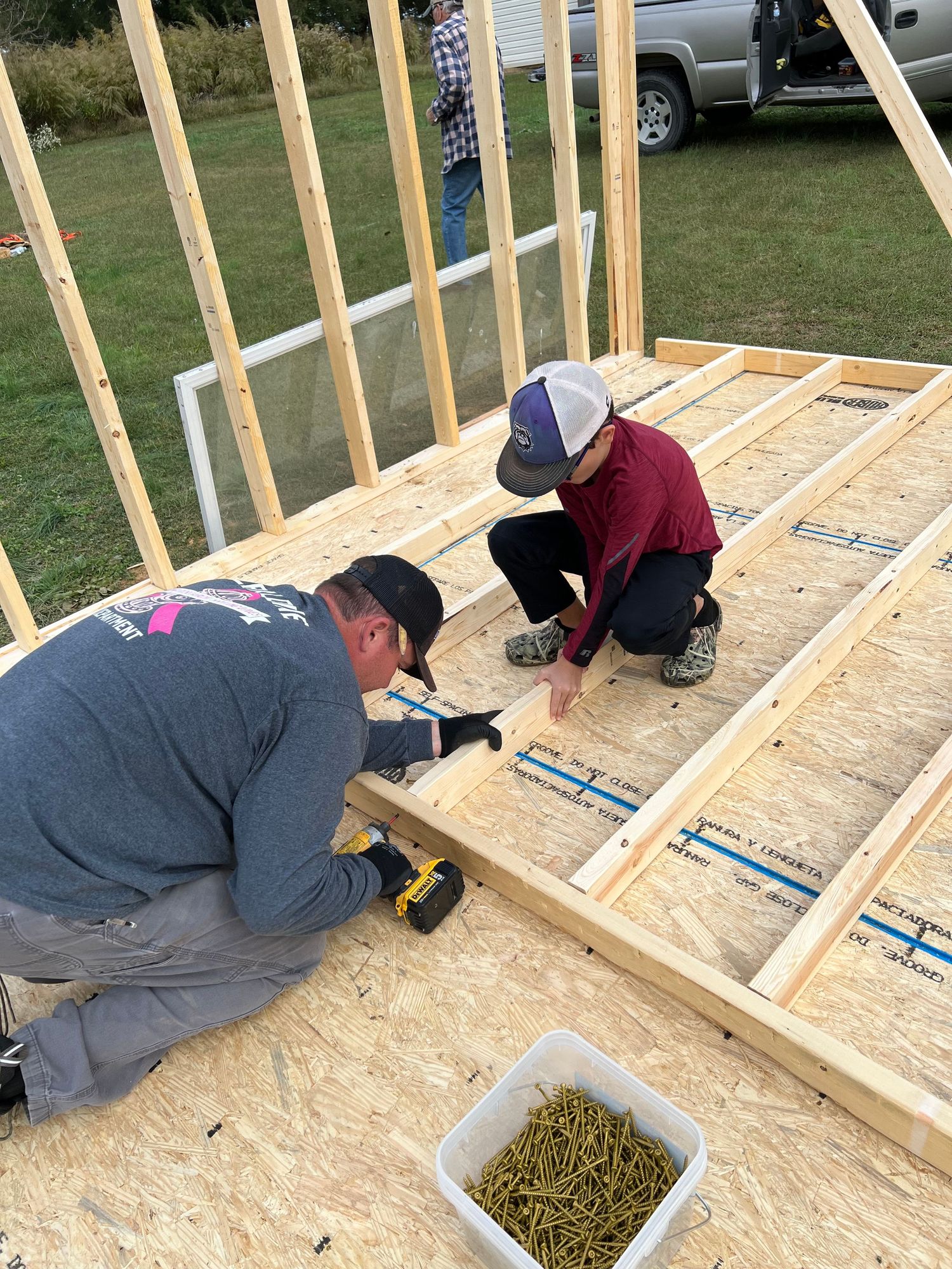 Construction worker installs floor joists while building a new wooden structure on plywood subfloor.