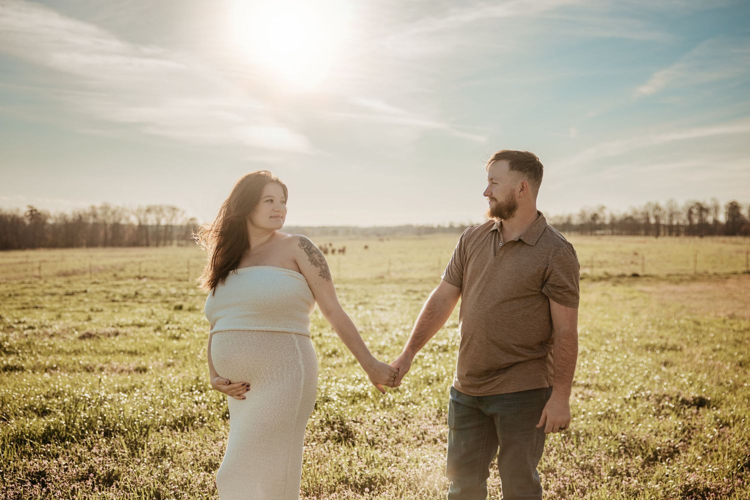 Couple holding hands while walking through sunny meadow at golden hour.