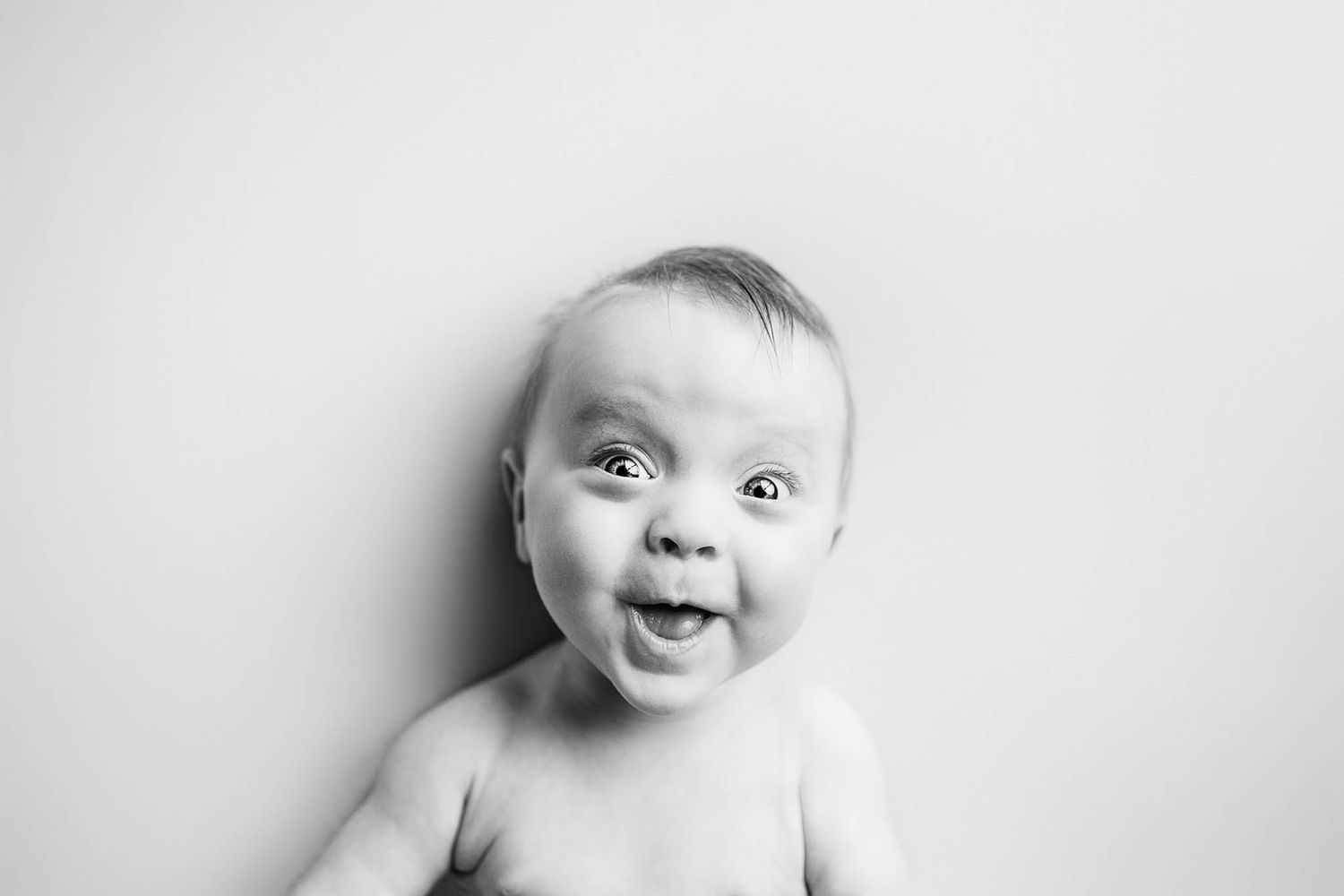 Black and white portrait of baby with expressive smile against white background.