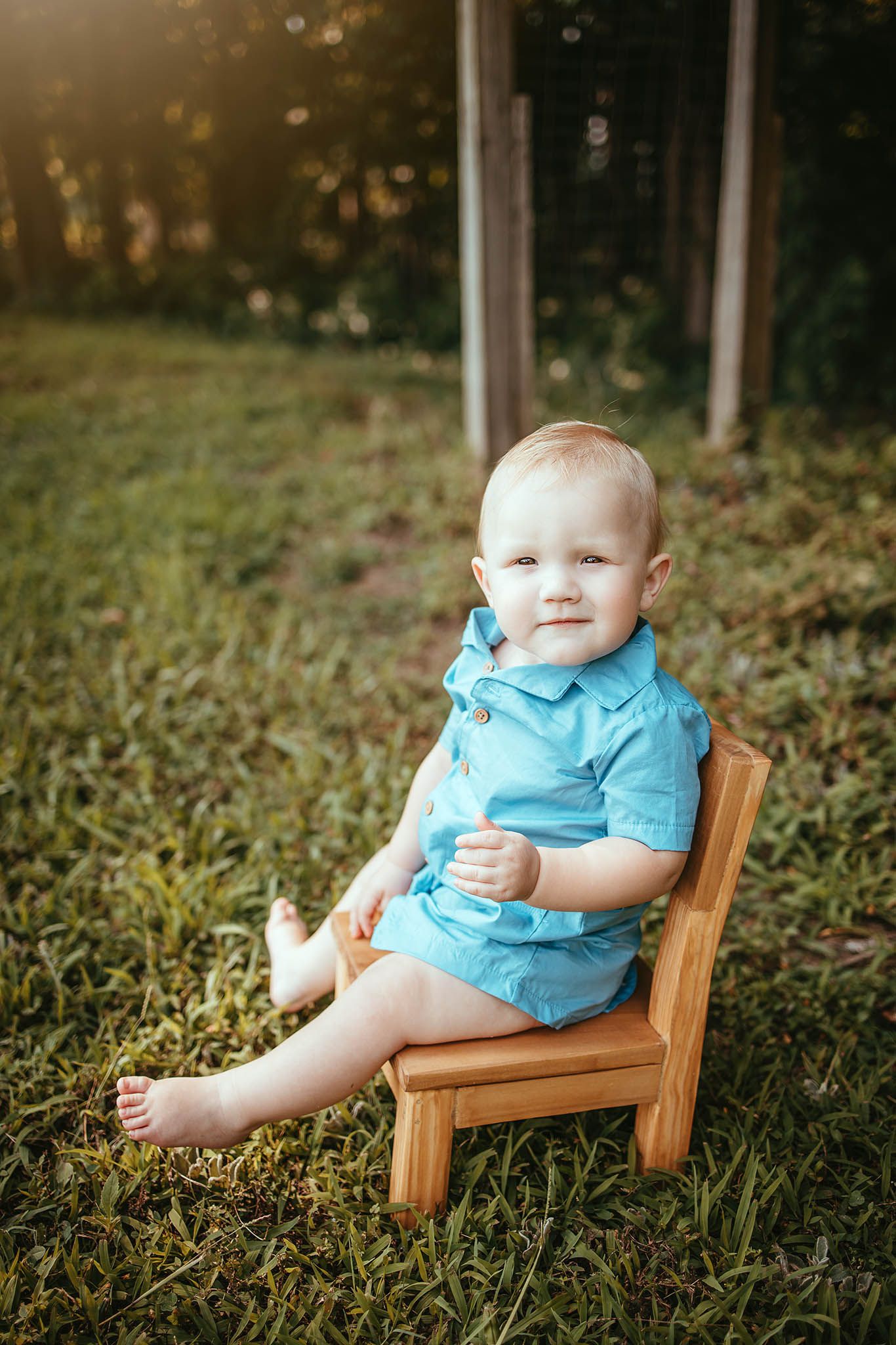 Baby in blue outfit sitting in wooden chair outdoors during golden hour.