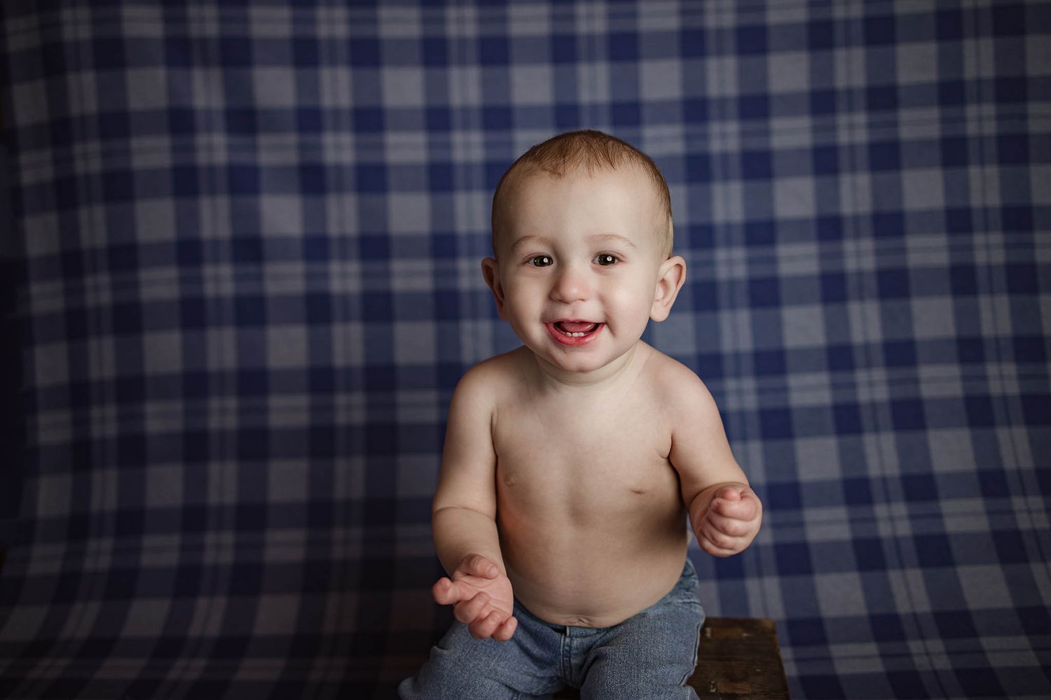 Happy baby against blue checkered background during milestone photo session.