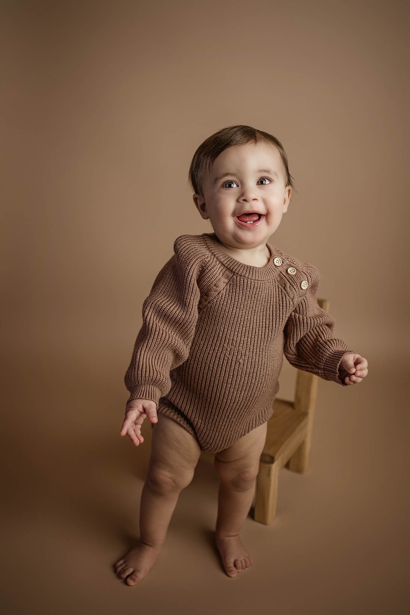 Infant wearing brown knit outfit playing with wooden furniture.