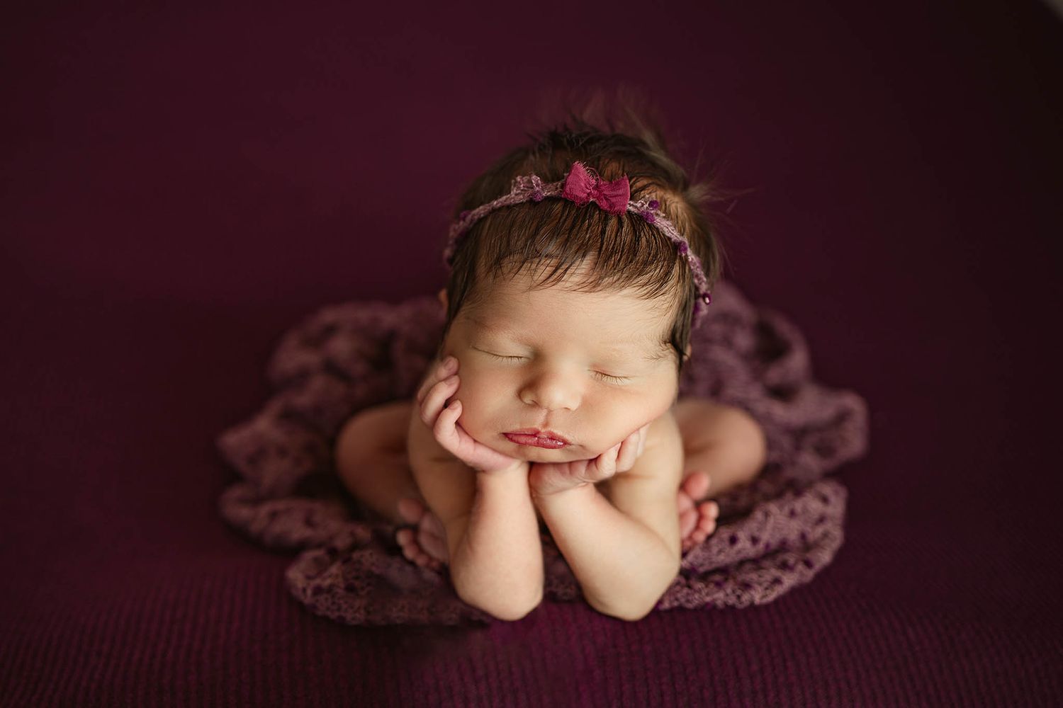 Artistic newborn portrait with deep purple tones and delicate lace details.