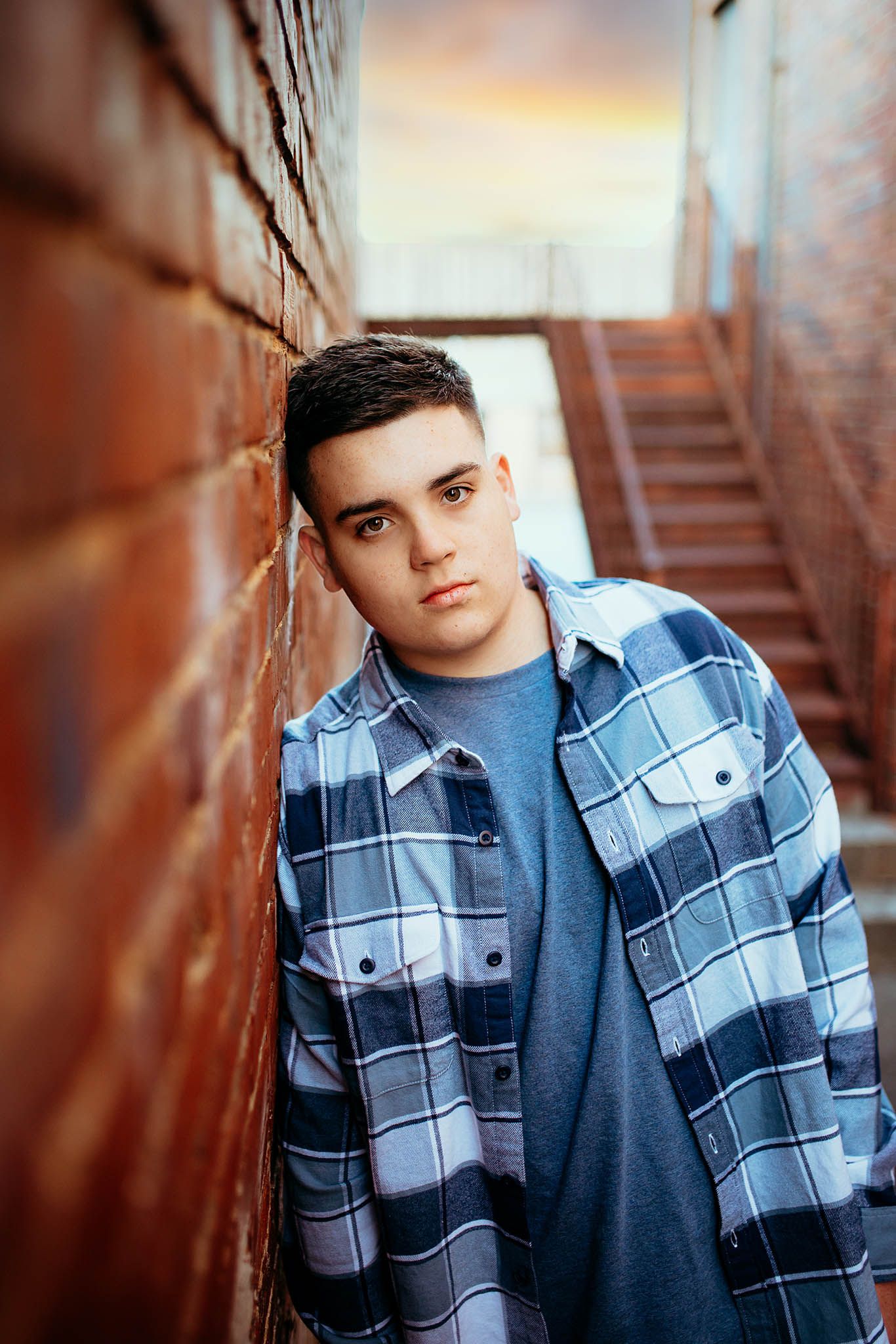Dramatic portrait against rustic brick wall in blue plaid jacket.