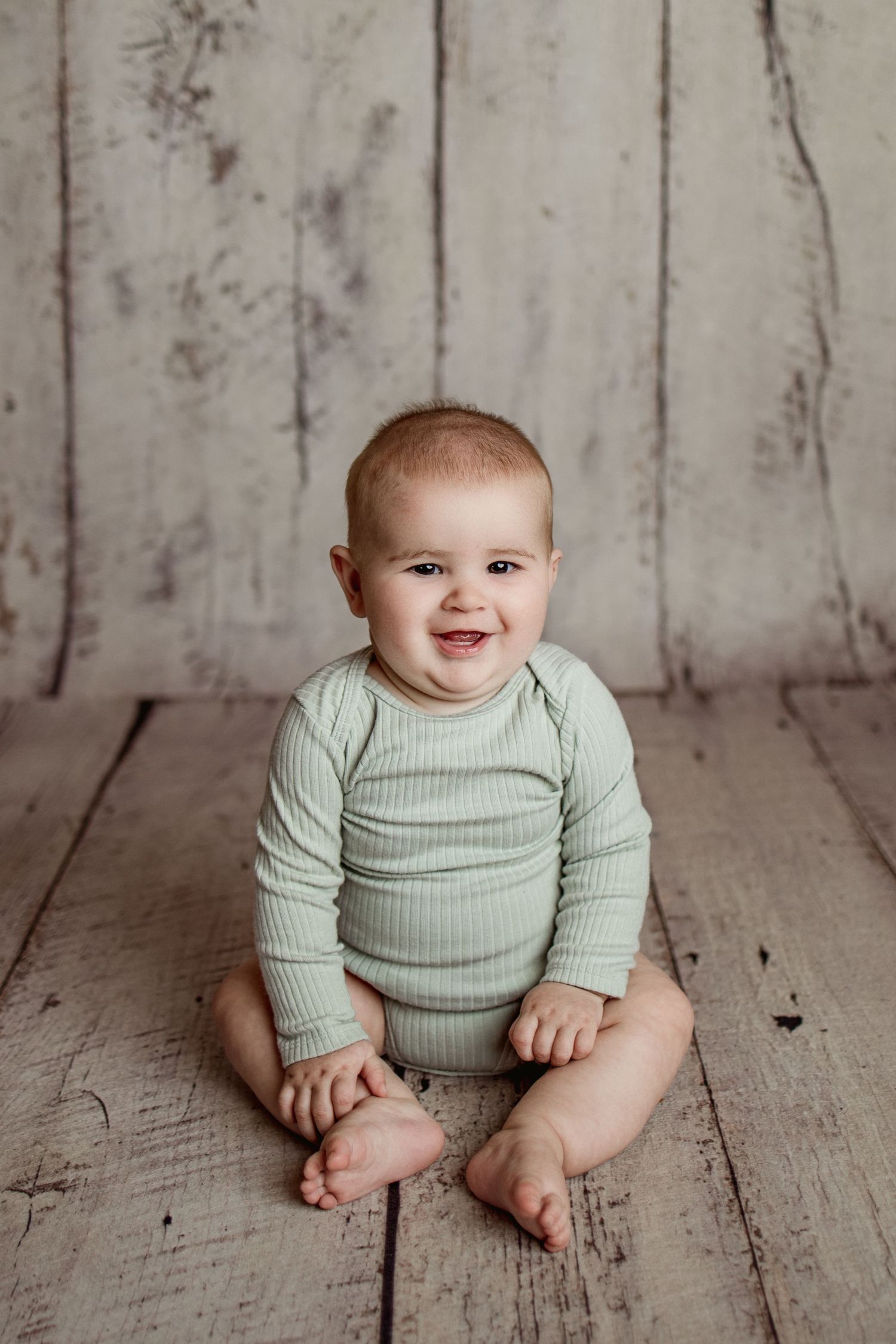 Sweet baby wearing mint green ribbed outfit sits on rustic wooden floor in progression of poses.