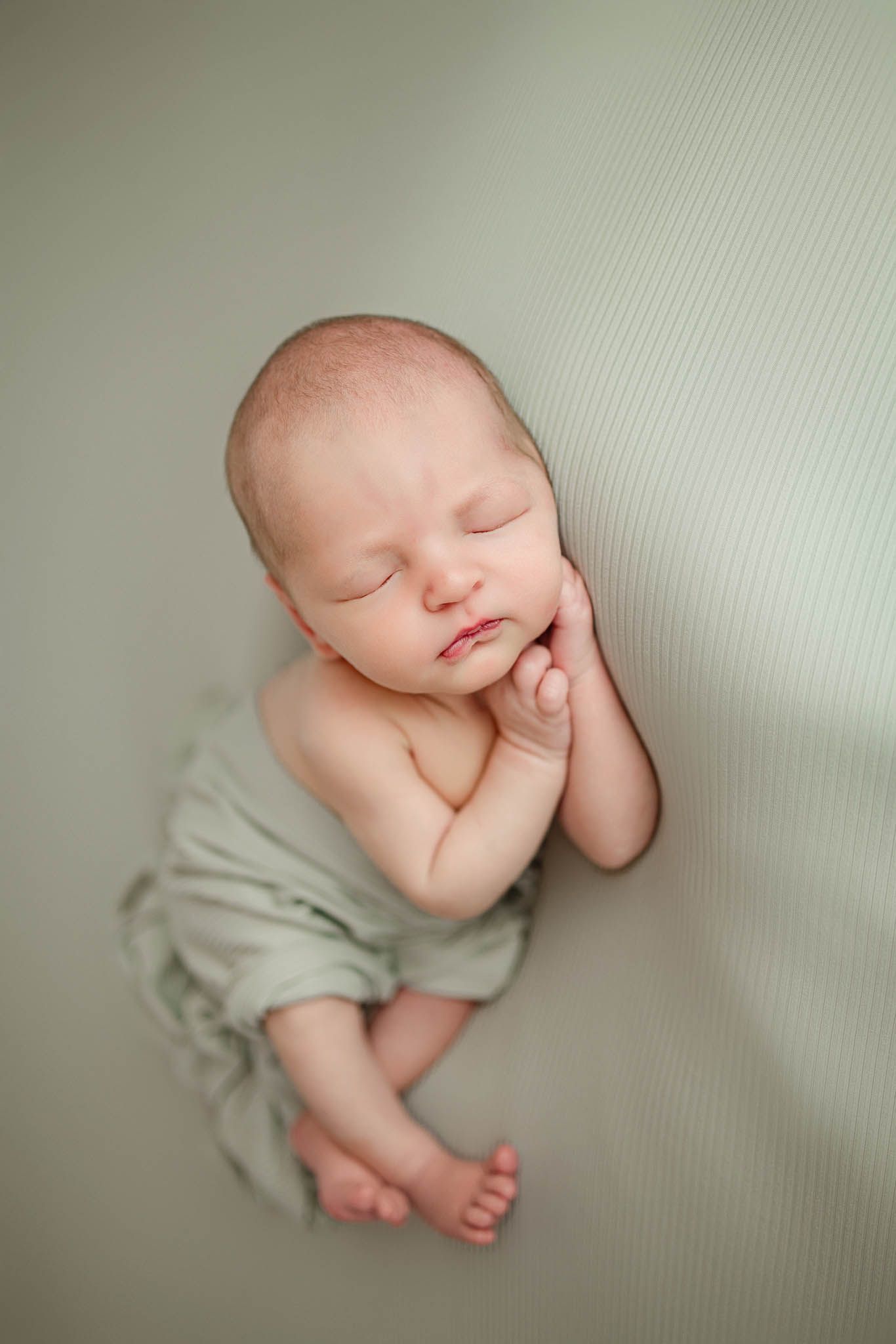 Peaceful sleeping newborn wrapped in light gray fabric on neutral background.