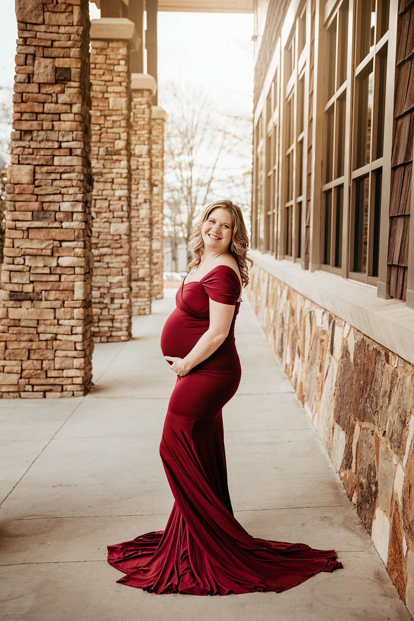 Elegant maternity session in a burgundy dress against stone architecture.