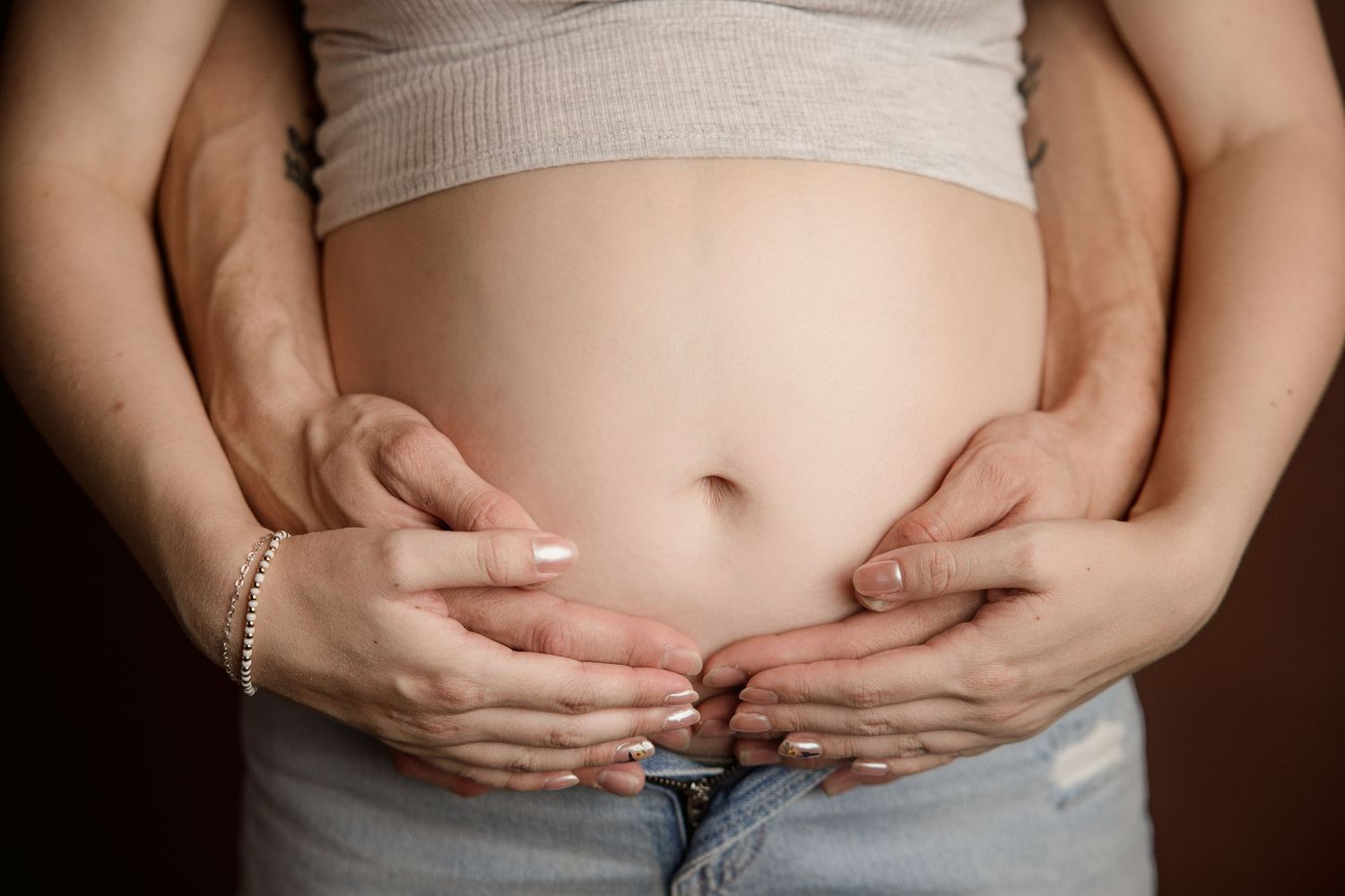 Series of photos showing hands cradling a pregnant belly against neutral background.