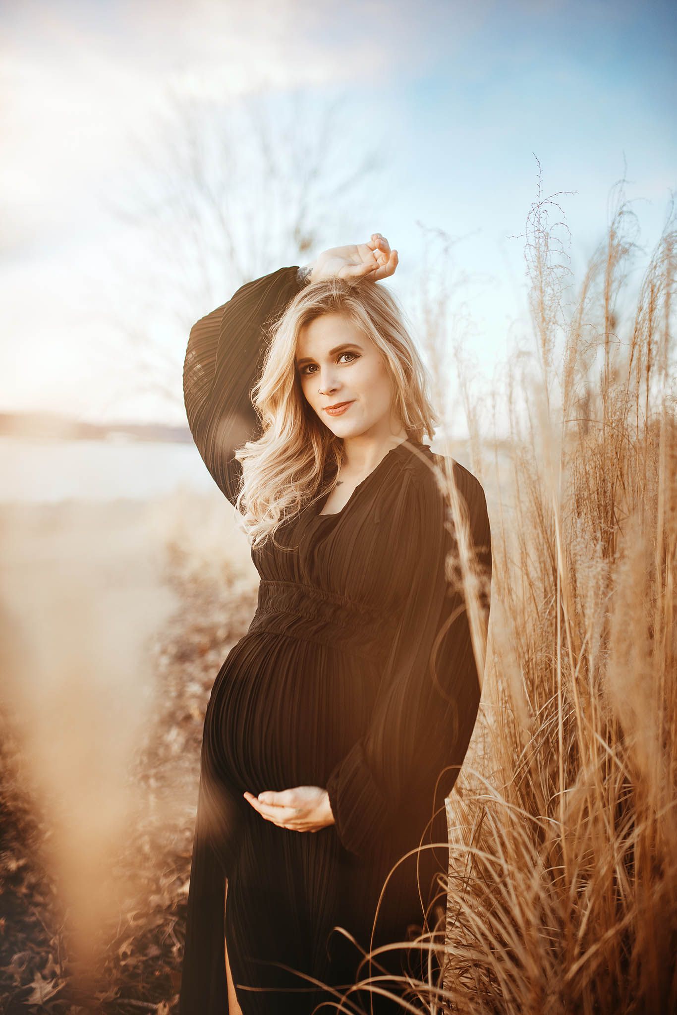 Artistic portrait of someone posing in a black sweater against dried tall grass during golden hour.