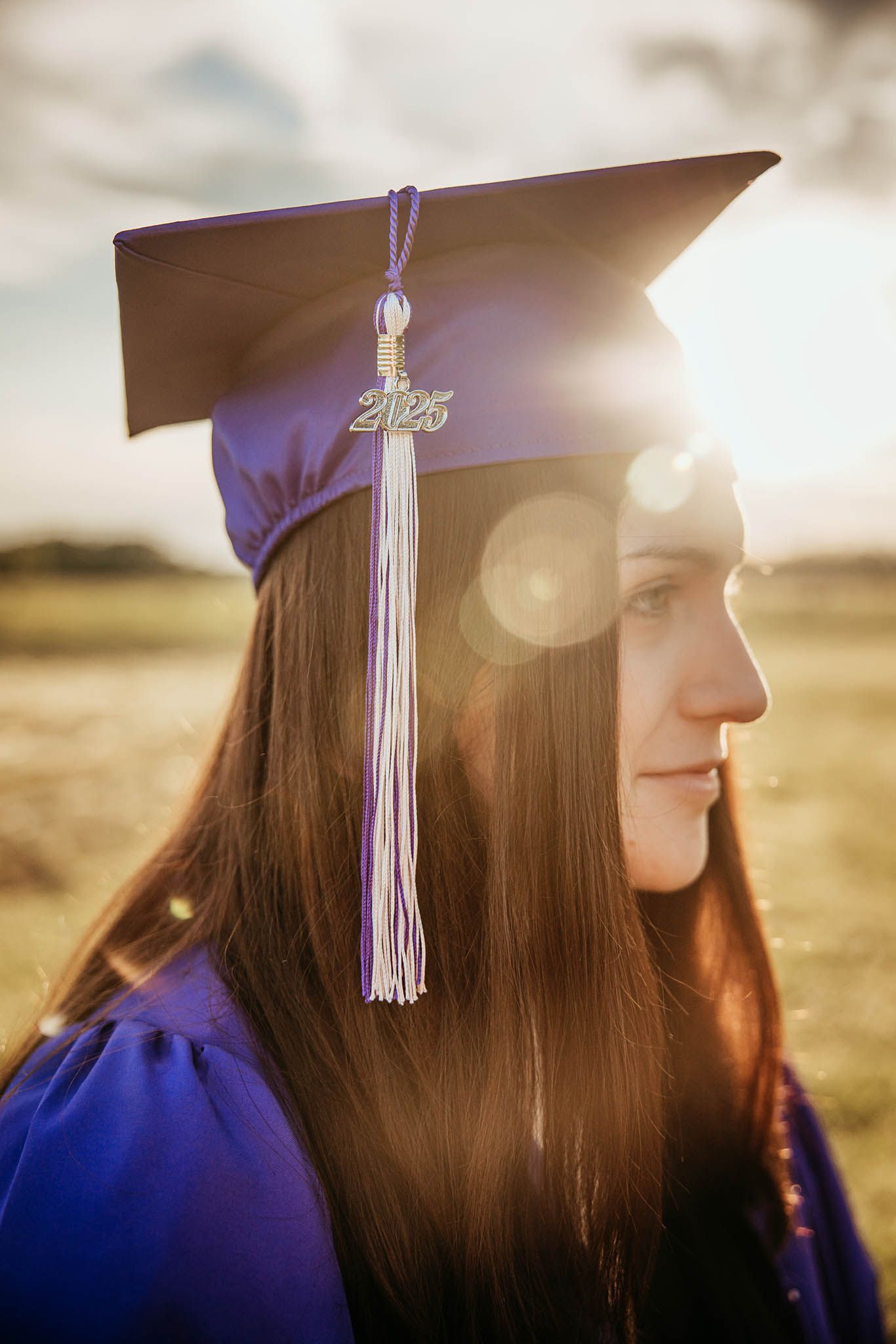 Profile view of a graduate in purple cap and gown with tassel against golden sunlight background.