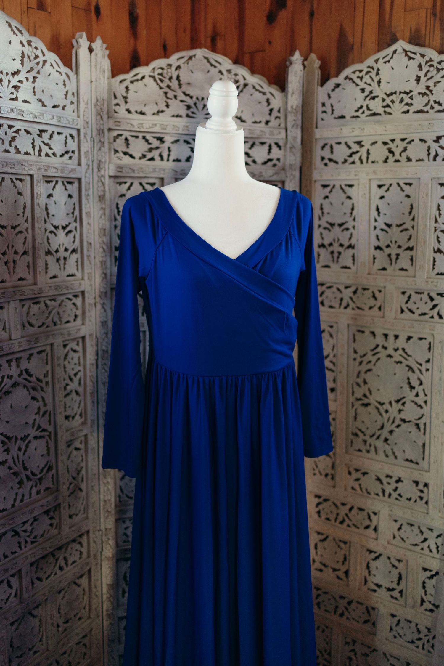 Royal blue empire waist dress with v-neckline and long sleeves displayed on white mannequin against ornate carved screen.