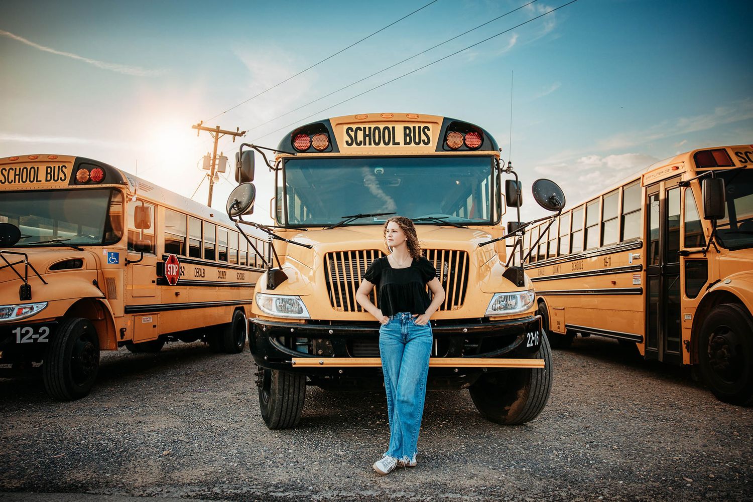 Row of yellow school buses parked in a parking lot against a blue sky.