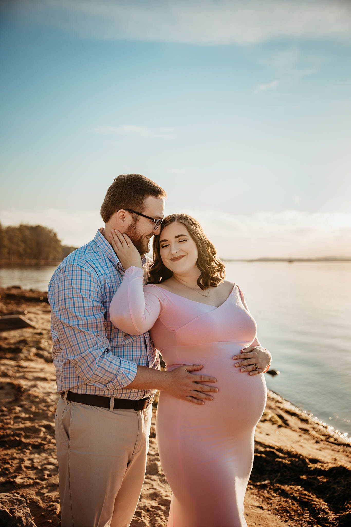 Romantic maternity photo of couple embracing on rocky beach at sunset.