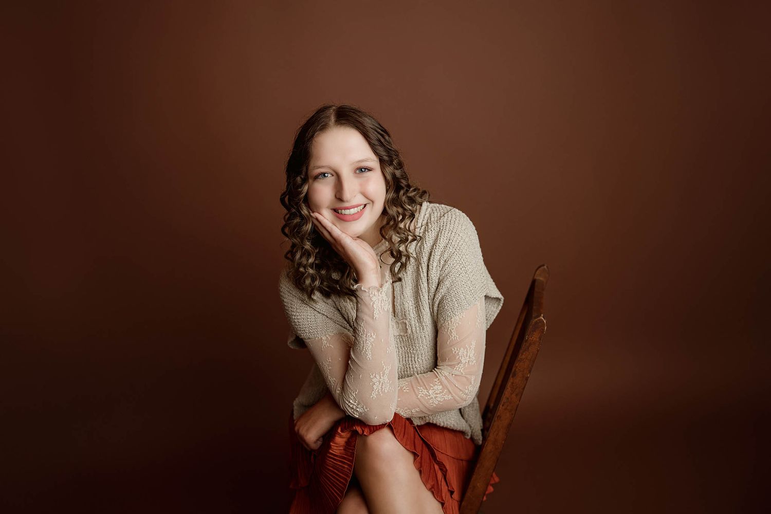 Studio portrait with warm brown backdrop and vintage wooden chair.