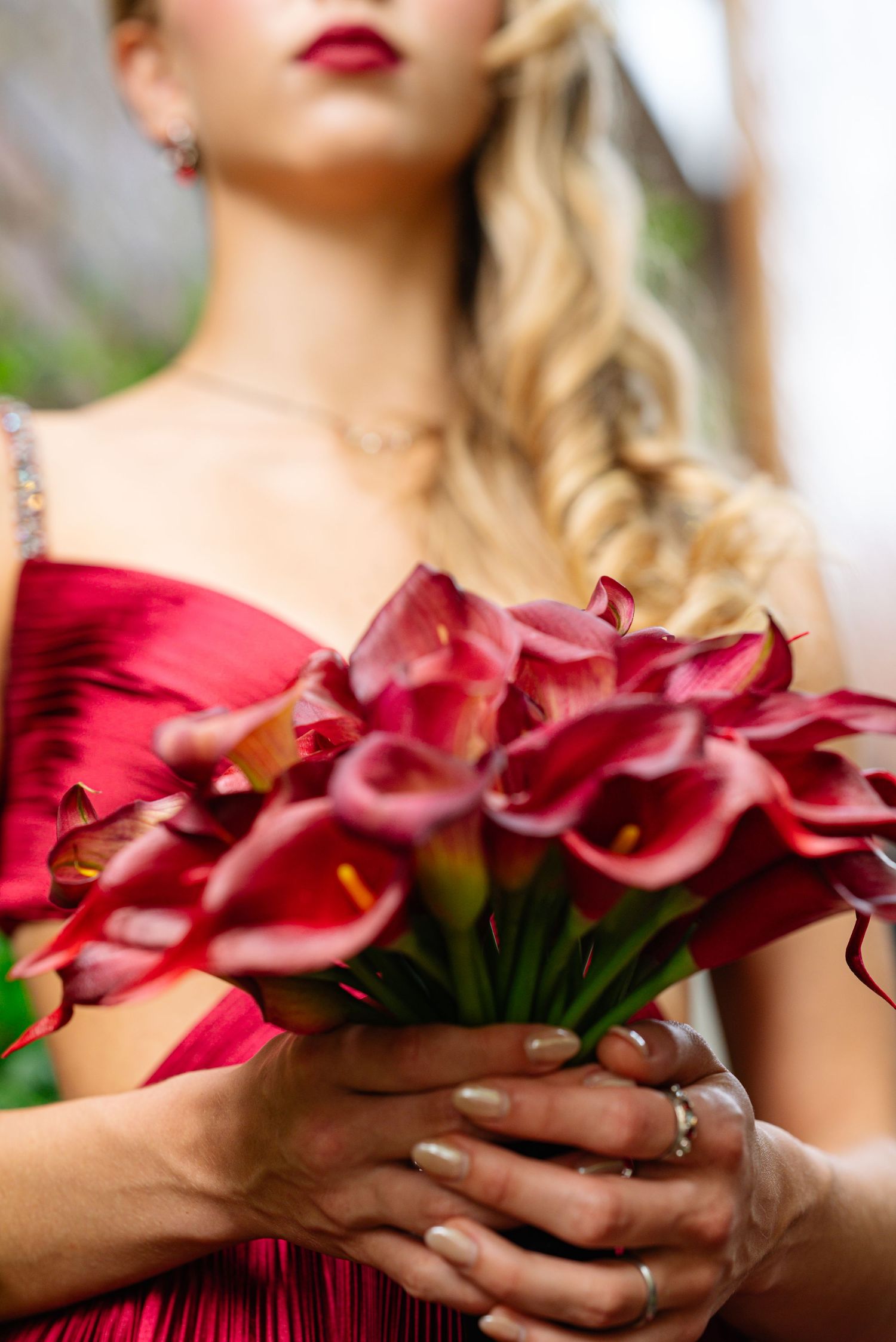 Pink calla lilies held against red formal dress with elegant styling.