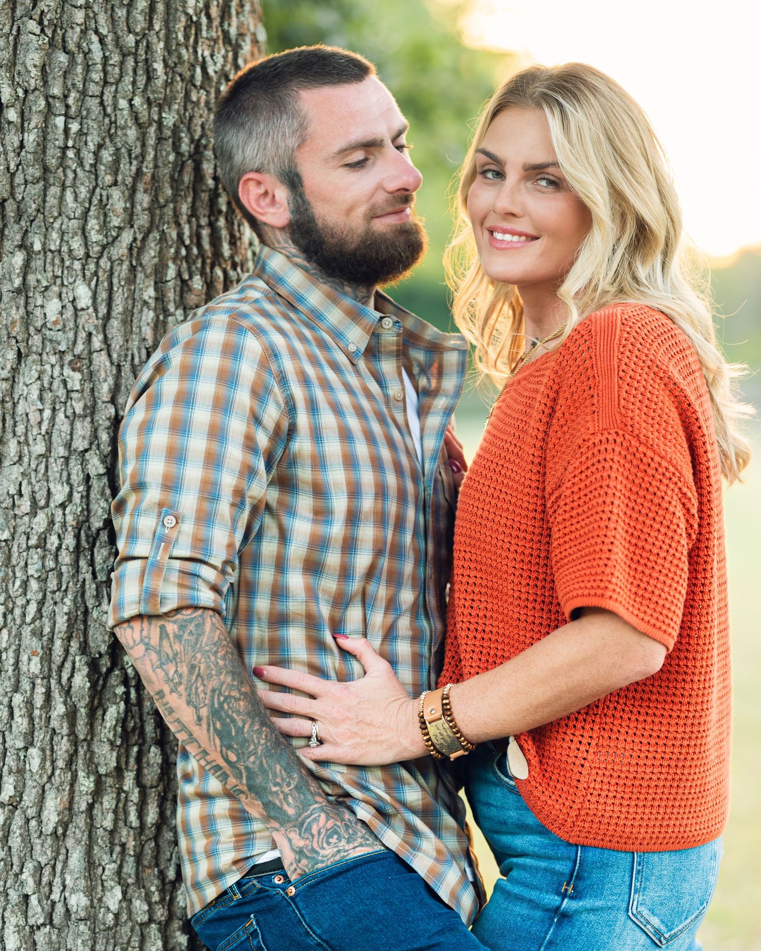 Couple sharing intimate moments against tree trunk in warm sunset light.