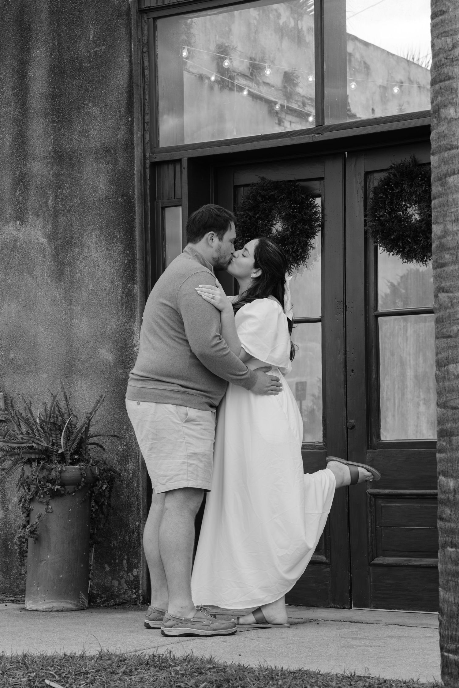 A black and white romantic moment captured outside a vintage storefront.