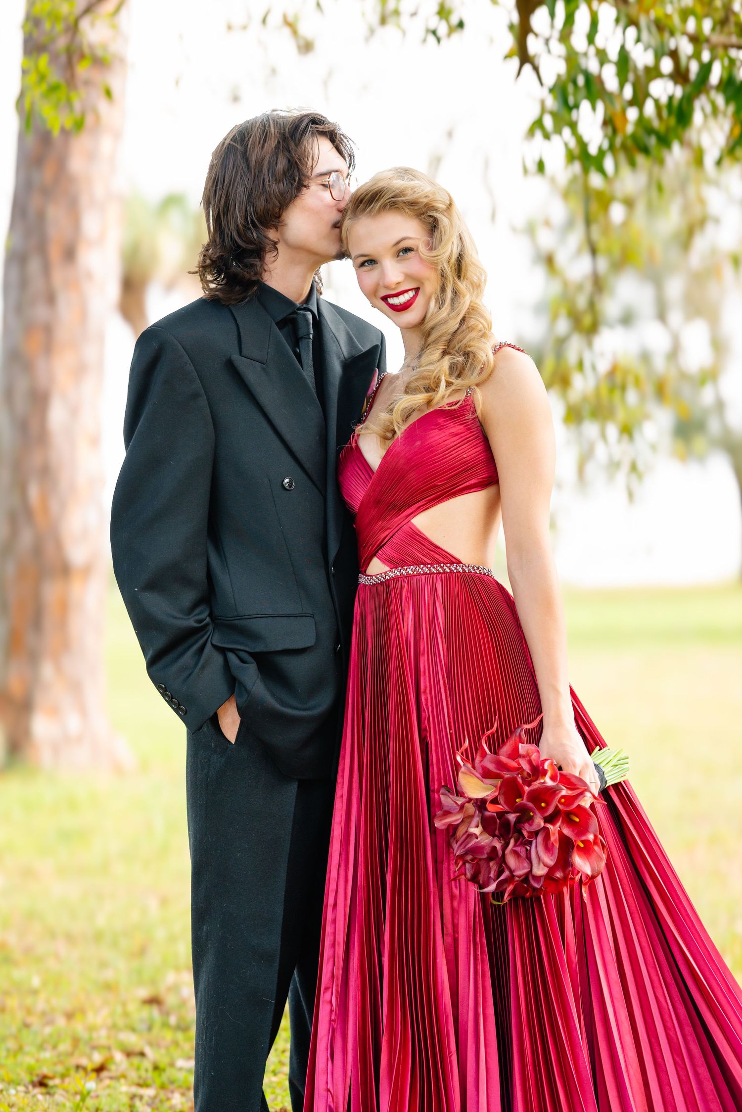 Couple in formal attire sharing intimate moments in a sunlit garden setting.