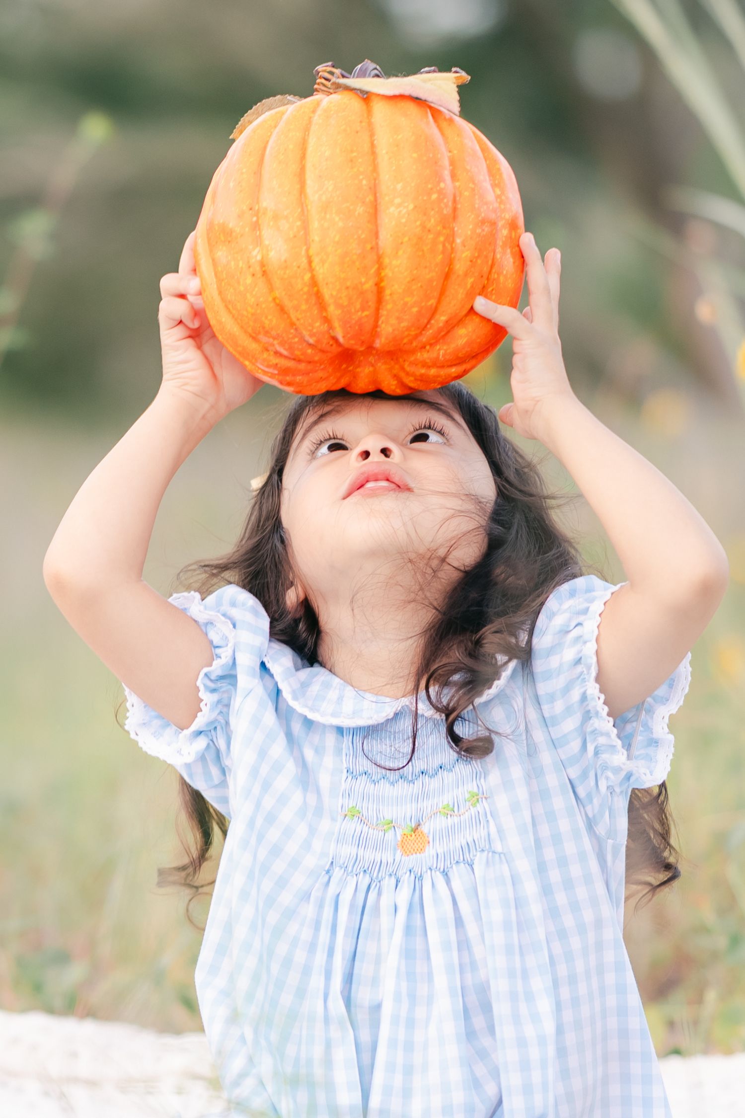 A playful sequence of a child holding an orange pumpkin overhead in a blue dress.