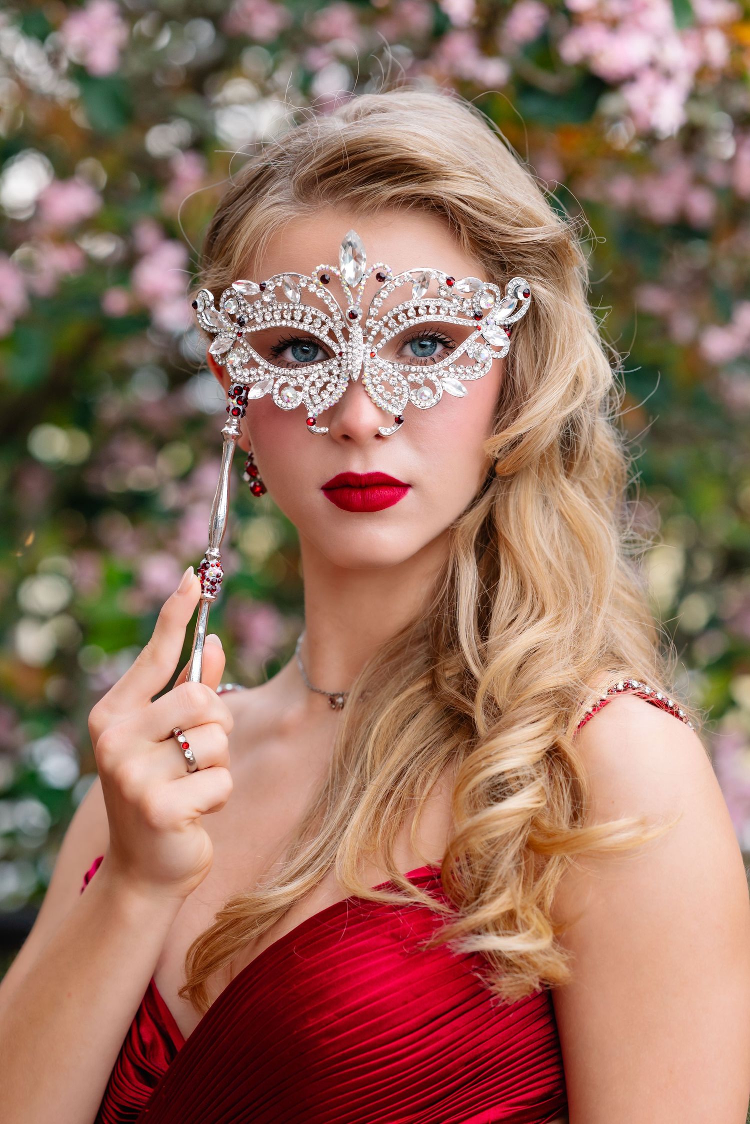 Glamorous portrait with decorative crystal mask against pink blossoms.