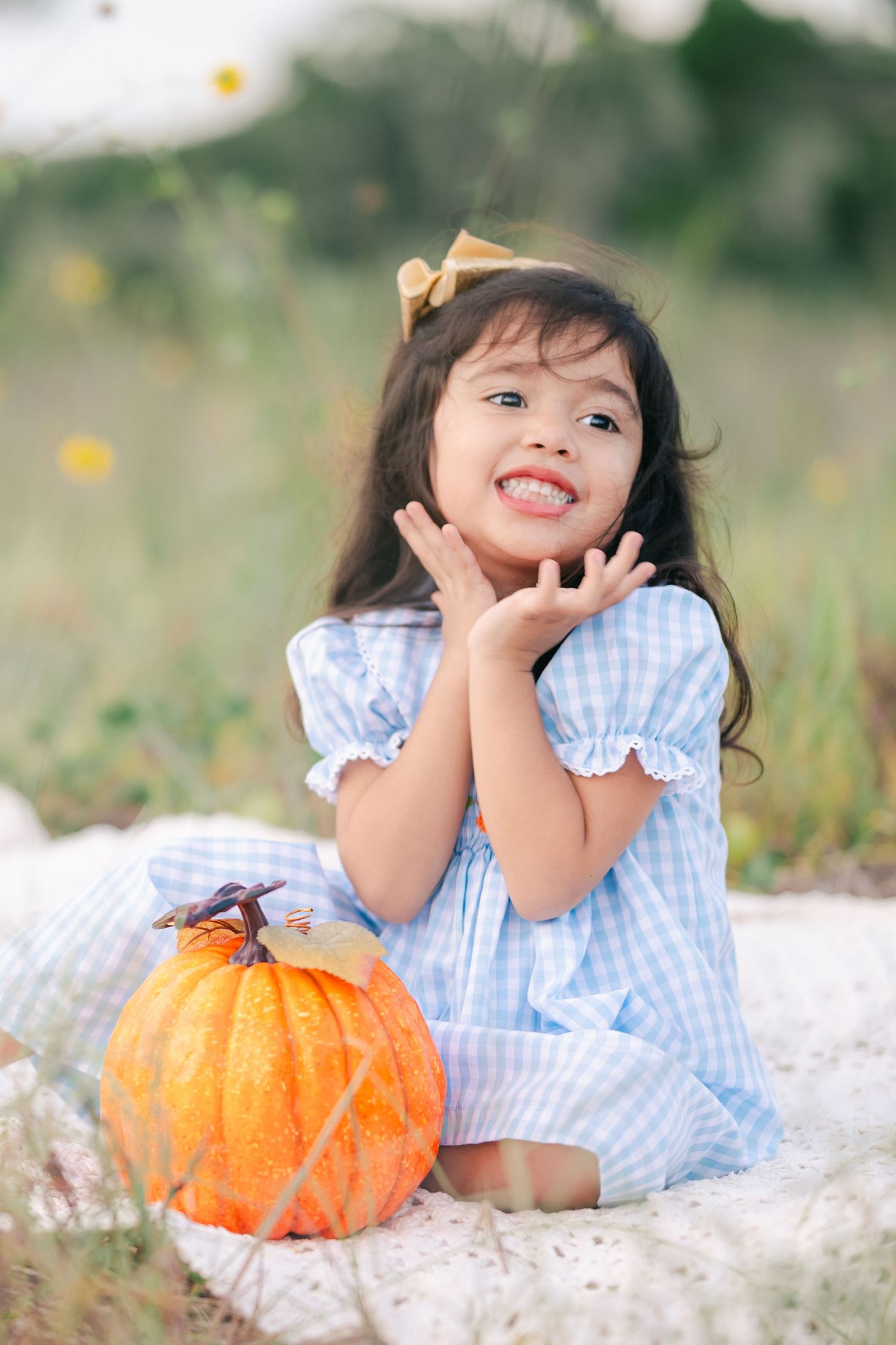 A child in gingham poses with a pumpkin during an autumn outdoor photoshoot.