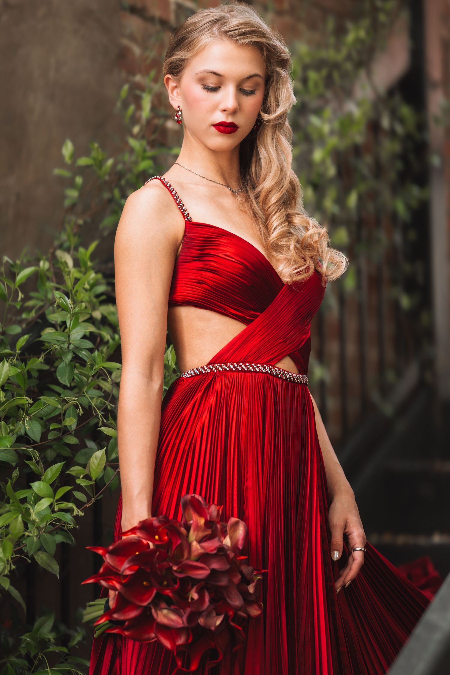 Stunning red velvet gown with pleated details and floral accents photographed in garden setting.