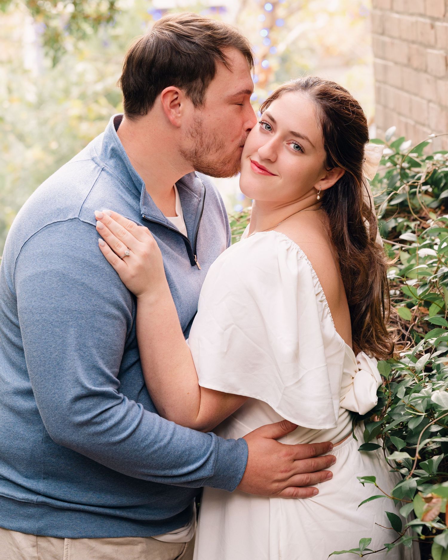 A romantic embrace captured in soft lighting against a brick wall backdrop.