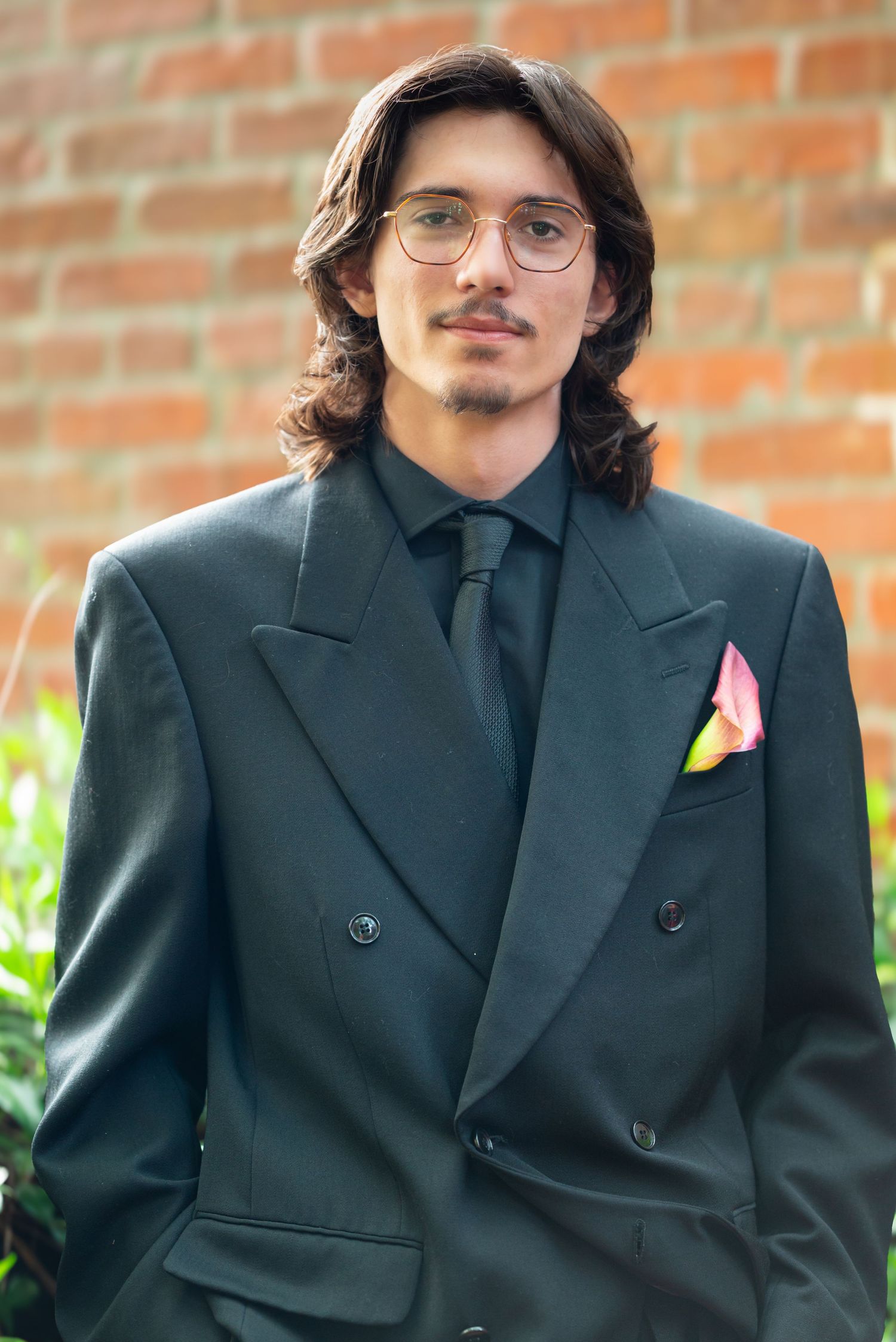 Portrait series of person in classic black suit and glasses against brick wall background.