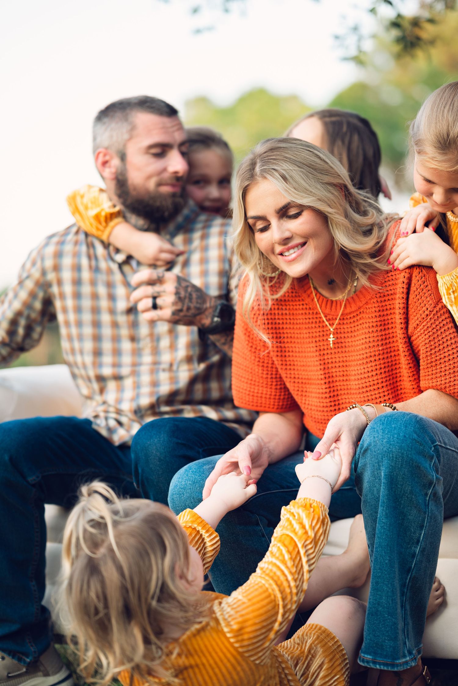 Family members in casual attire share playful moment on outdoor bench.