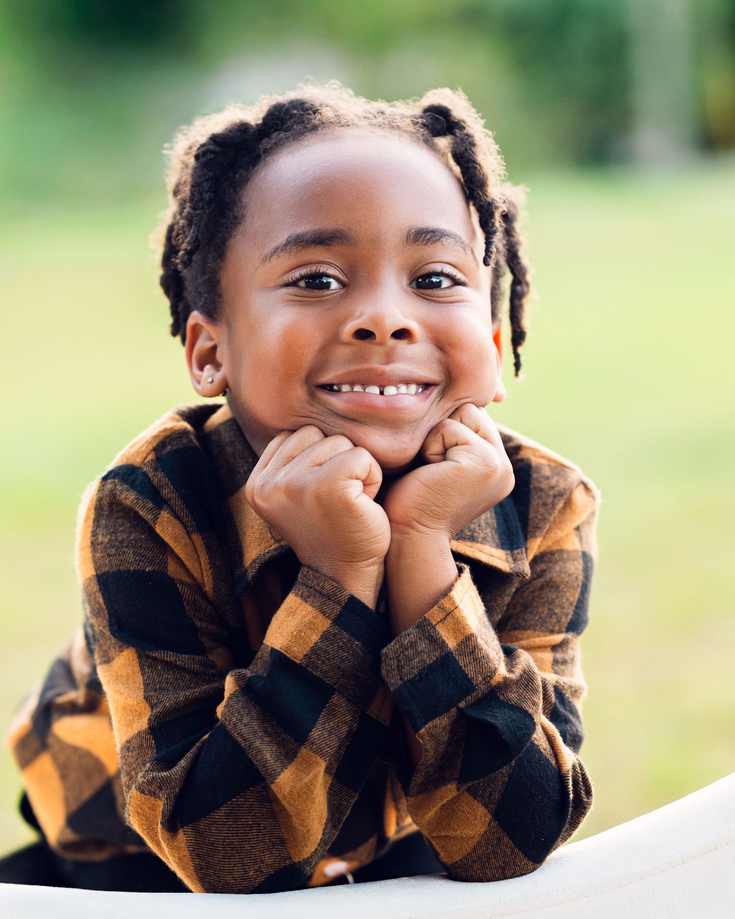 A child in a plaid flannel shirt poses with hands under chin for fall portrait.