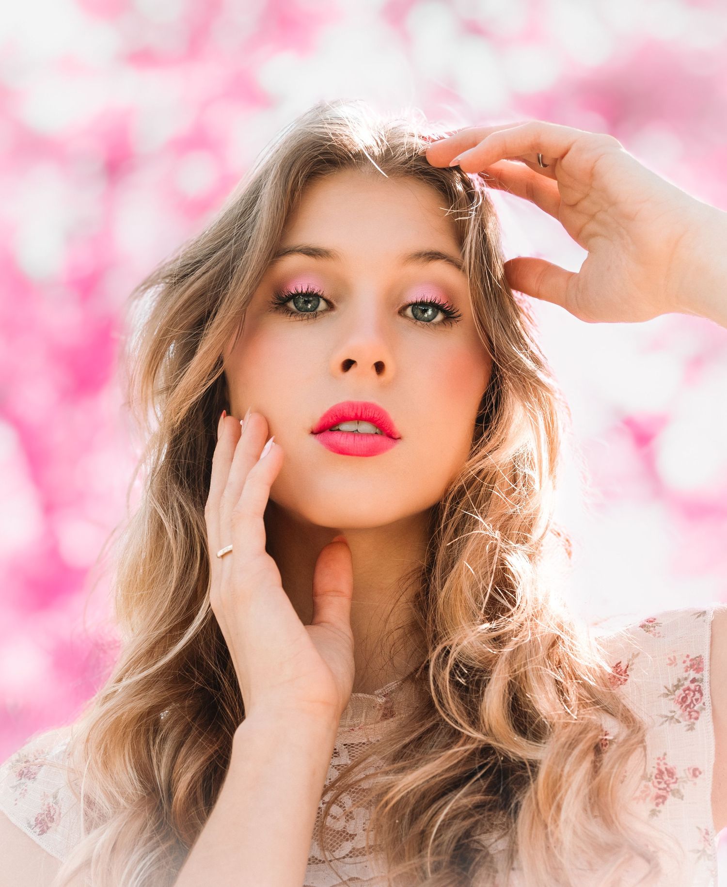 A portrait of a woman with wavy blonde hair and red lipstick against a pink floral background.