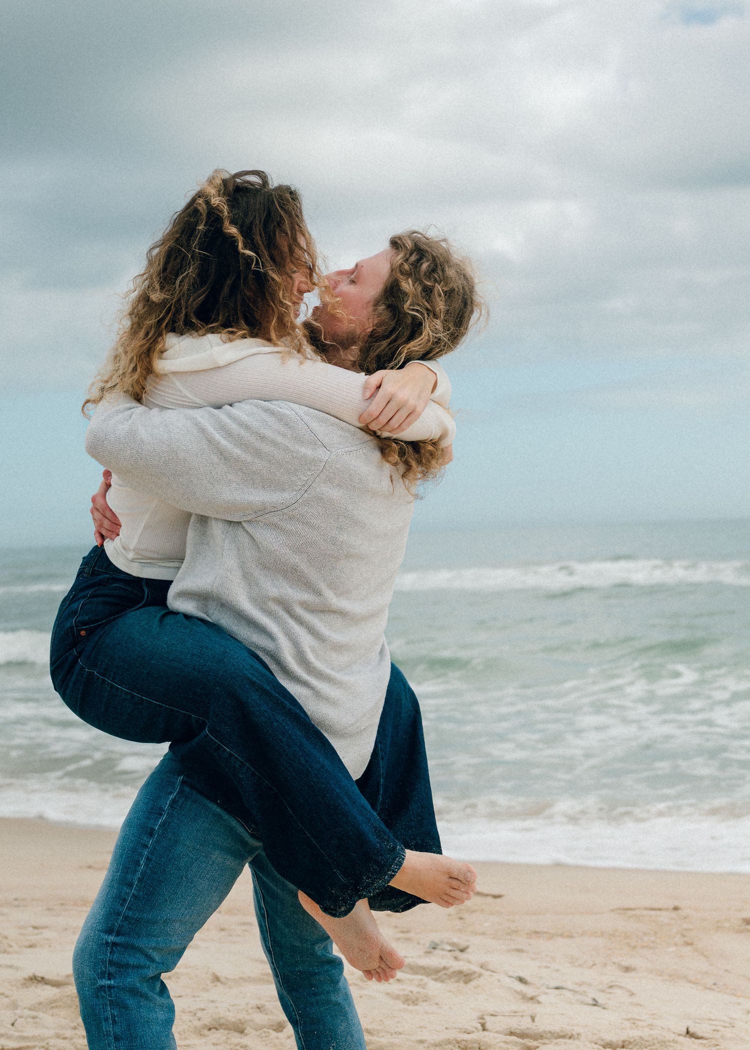 Romantic couple embracing and kissing in sequence of photos on a cloudy beach with crashing waves in the background.
