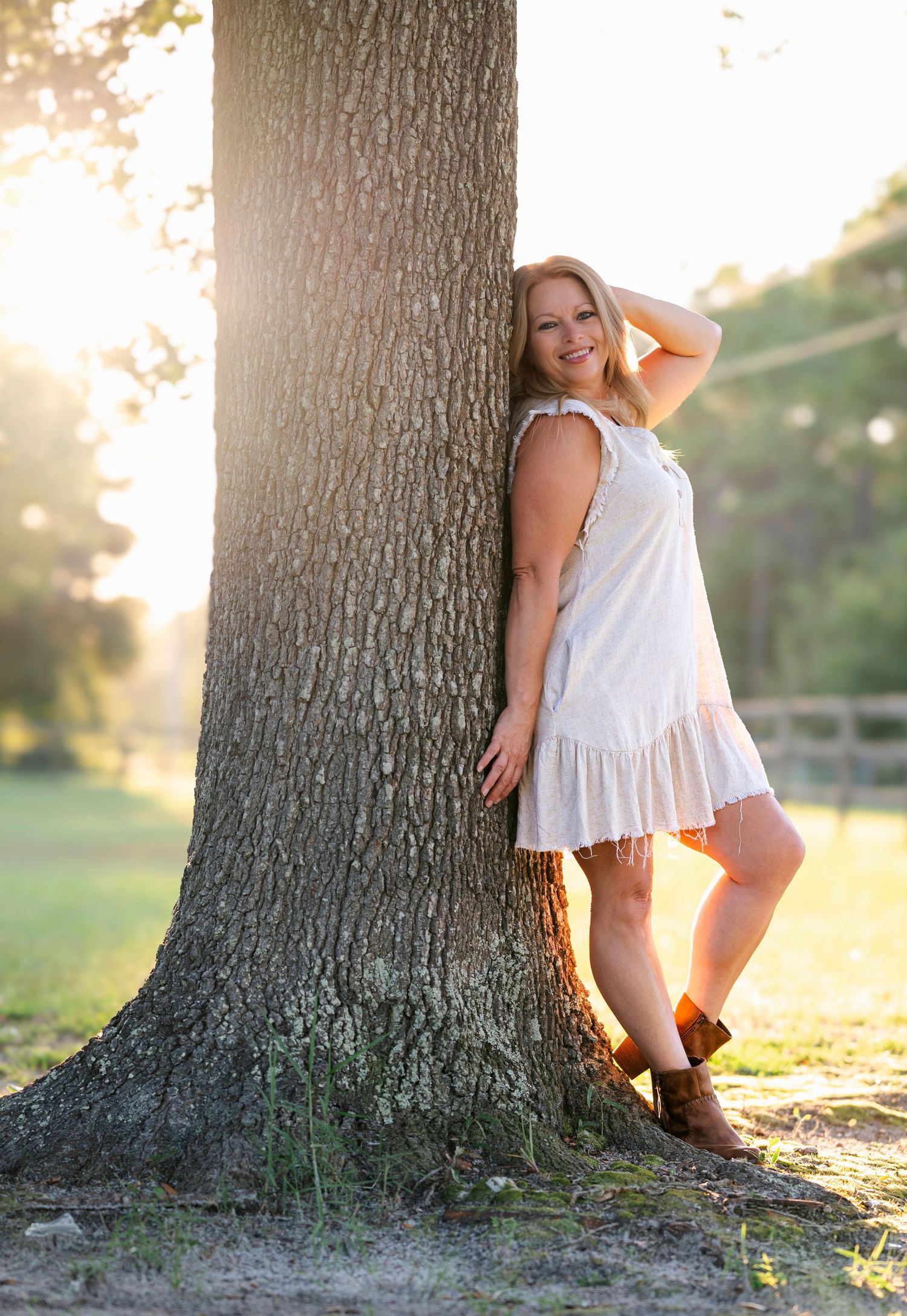 Rustic outdoor portrait session by a large tree trunk in a white summer dress.