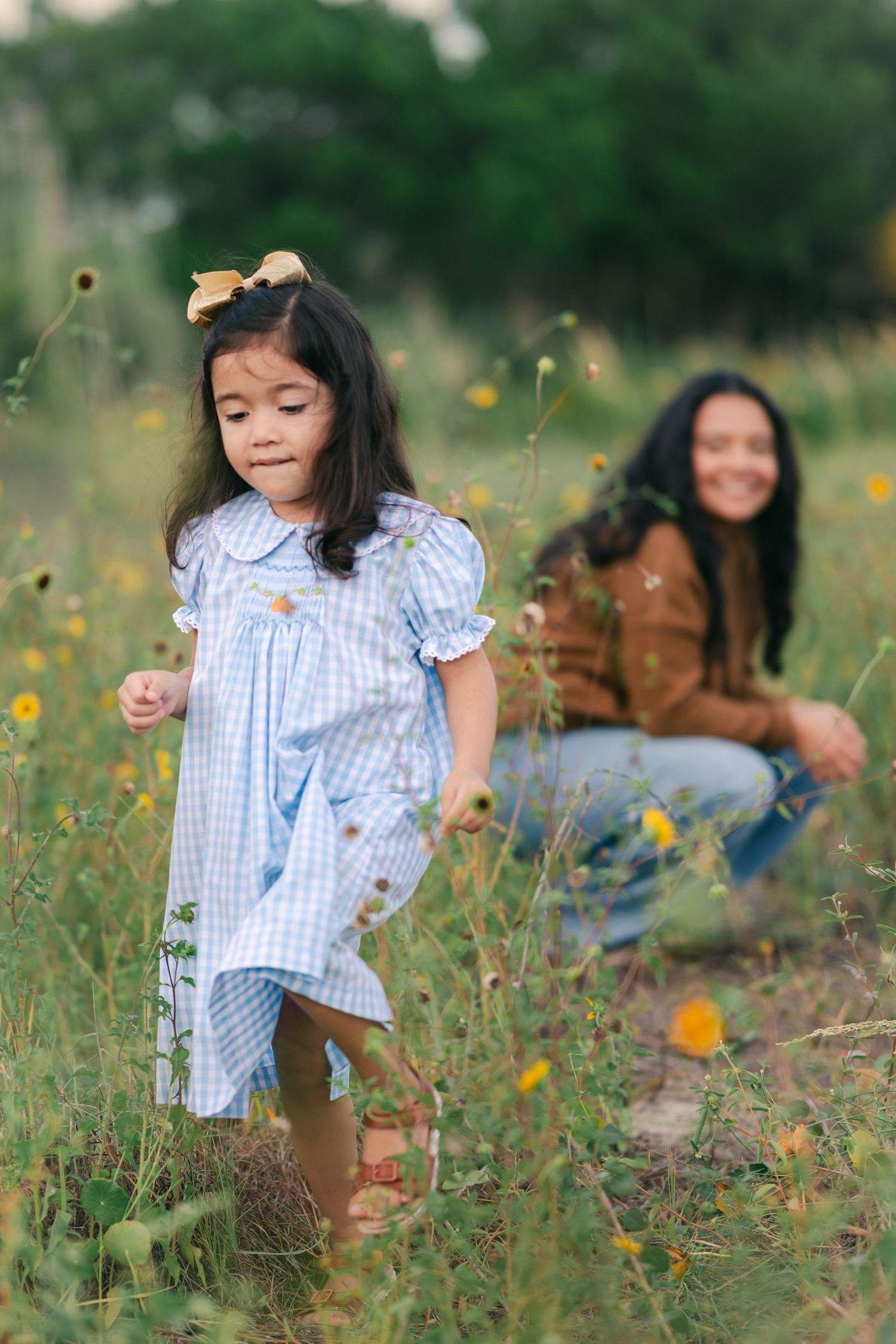 A playful scene in a wildflower meadow with a blue gingham dress and brown sweater.